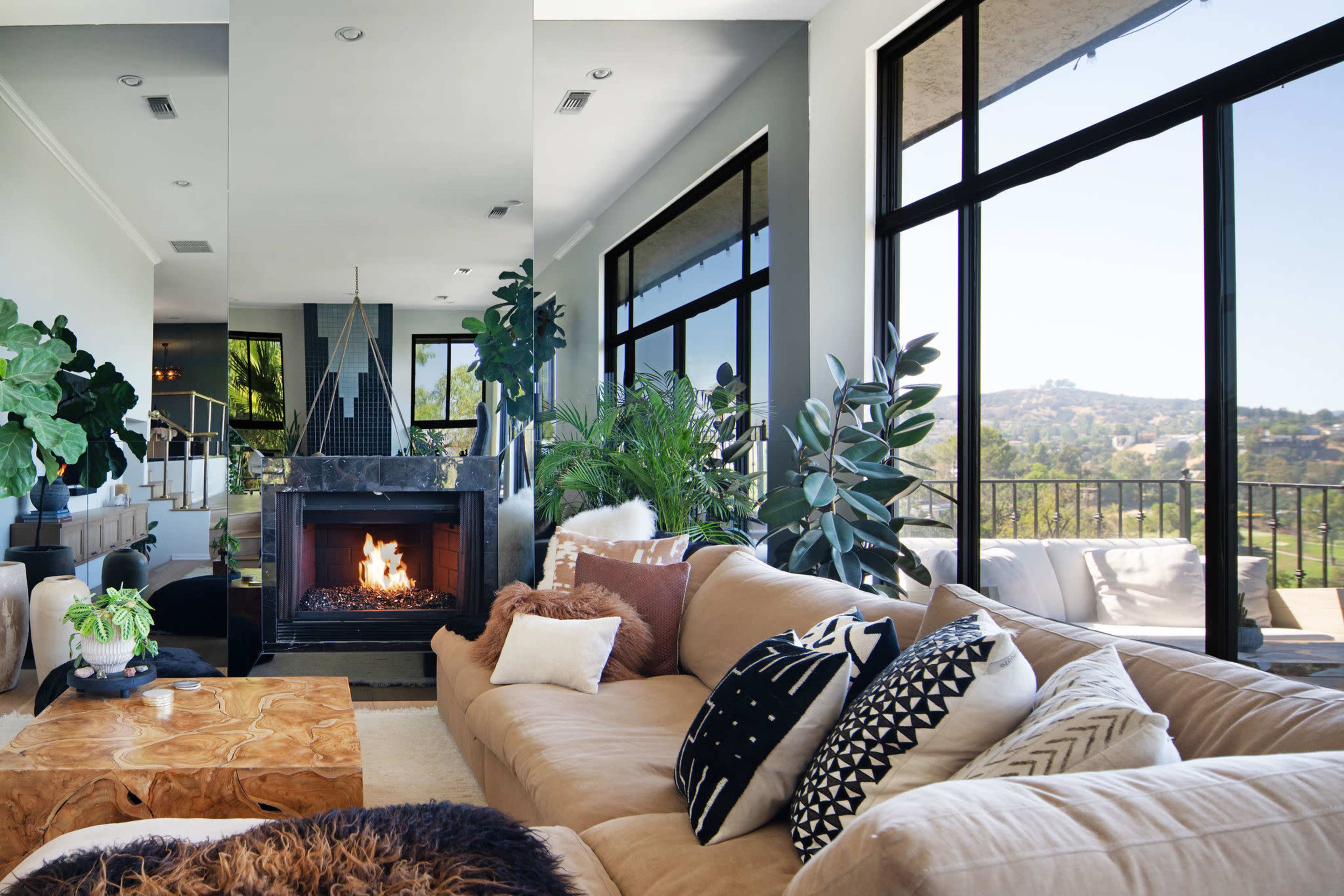 A spacious living room features a large sectional sofa, a wooden coffee table, and a fireplace, with large windows offering a view of the outdoor landscape.