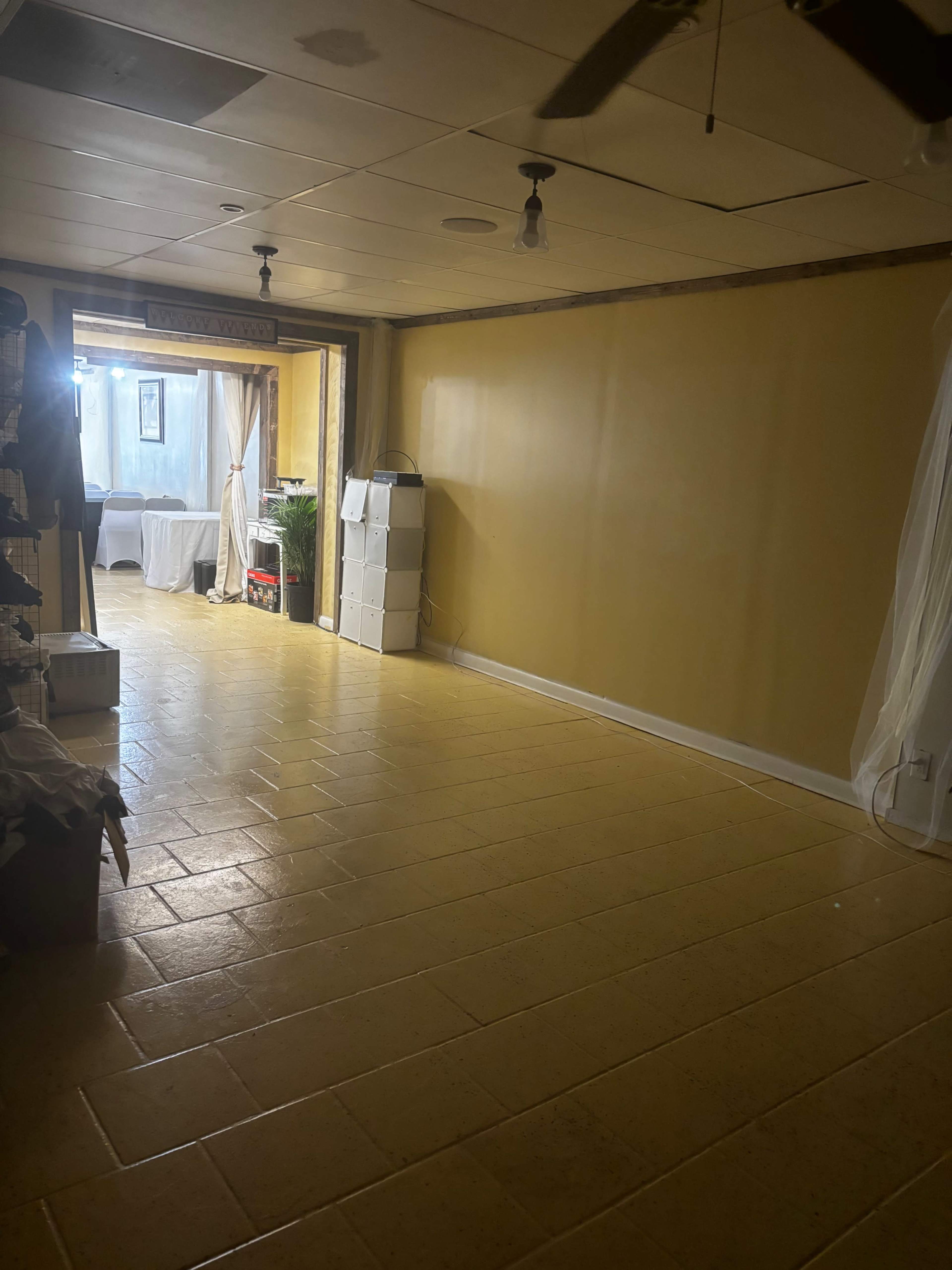 The image shows a mostly empty room with yellow walls, tiled flooring, and an entrance to another area at the far end.