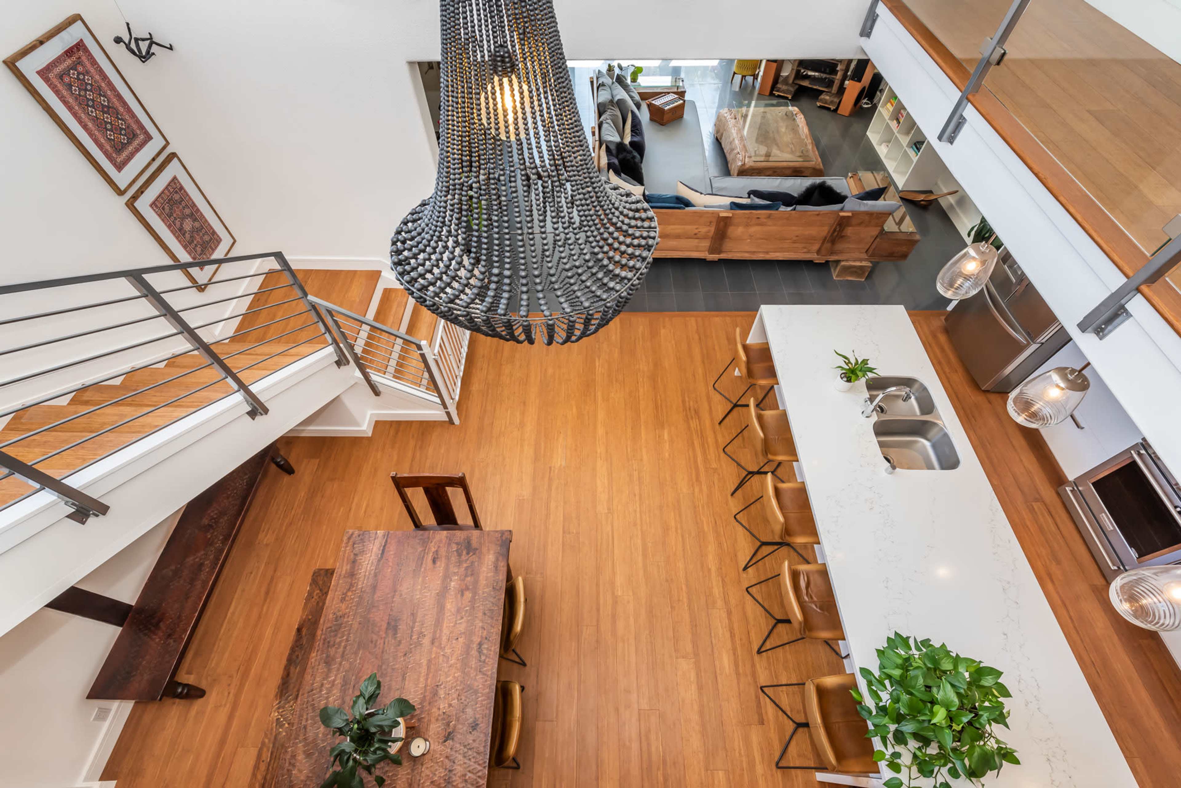 An open-concept living area featuring a long island bar, a dining table, and a modern chandelier, with a staircase leading to the upper level.