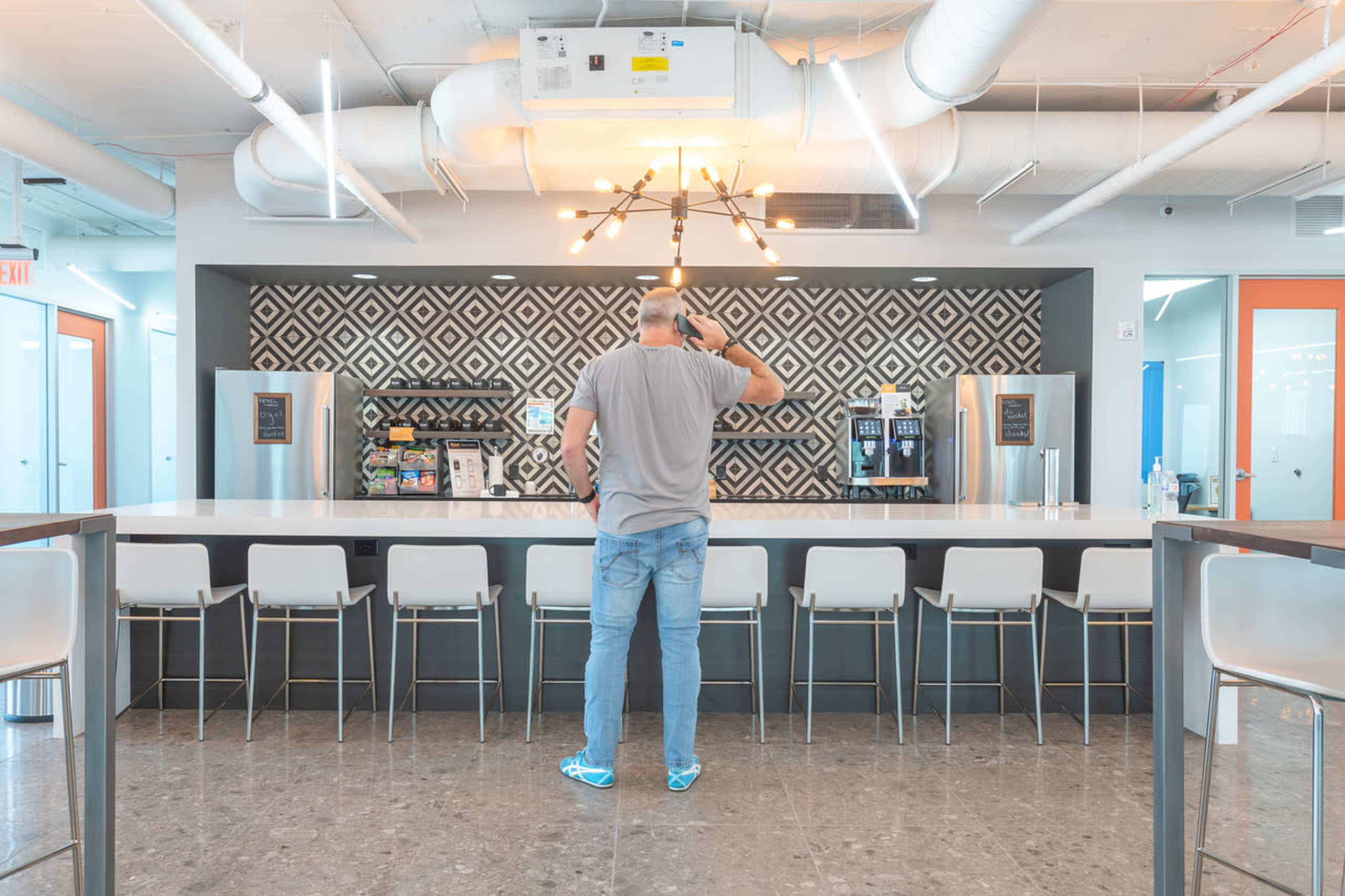 A man stands at a bar-style counter in a modern kitchen area, looking toward a wall decorated with geometric tiles.