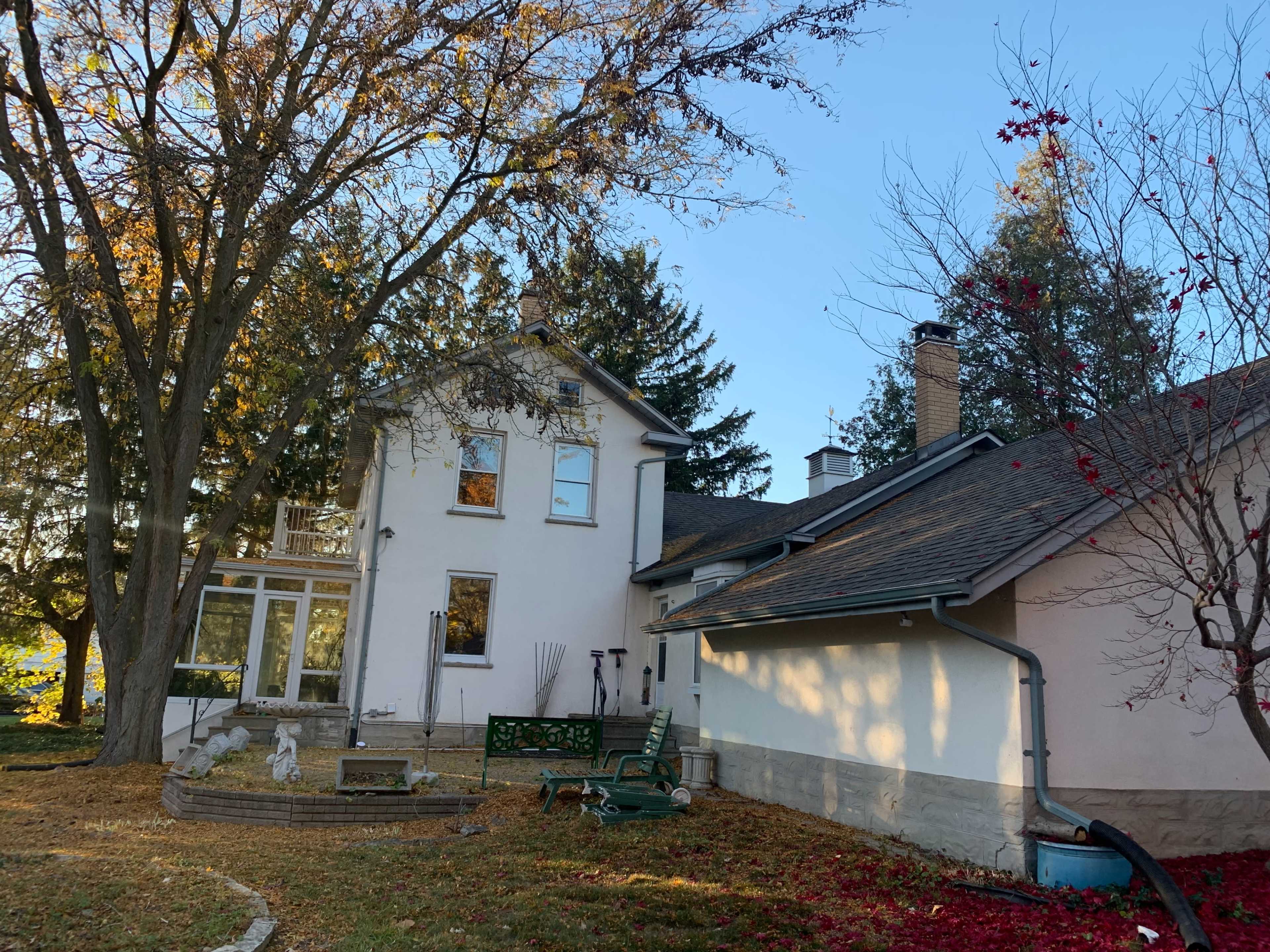 A two-story house surrounded by trees and a lawn scattered with fallen leaves.