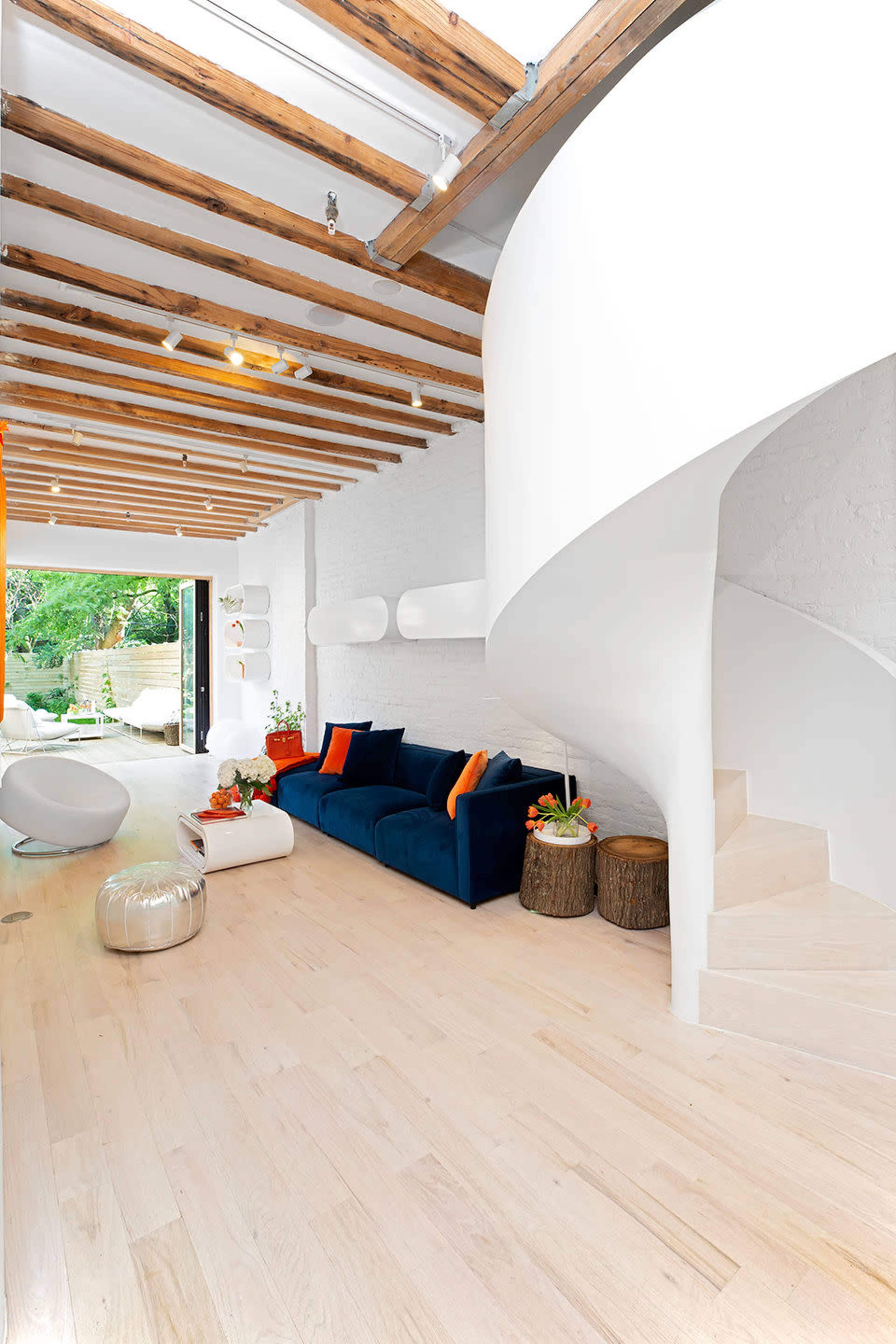 A modern living room featuring a navy blue sofa, a spiral staircase, and wooden beams overhead.