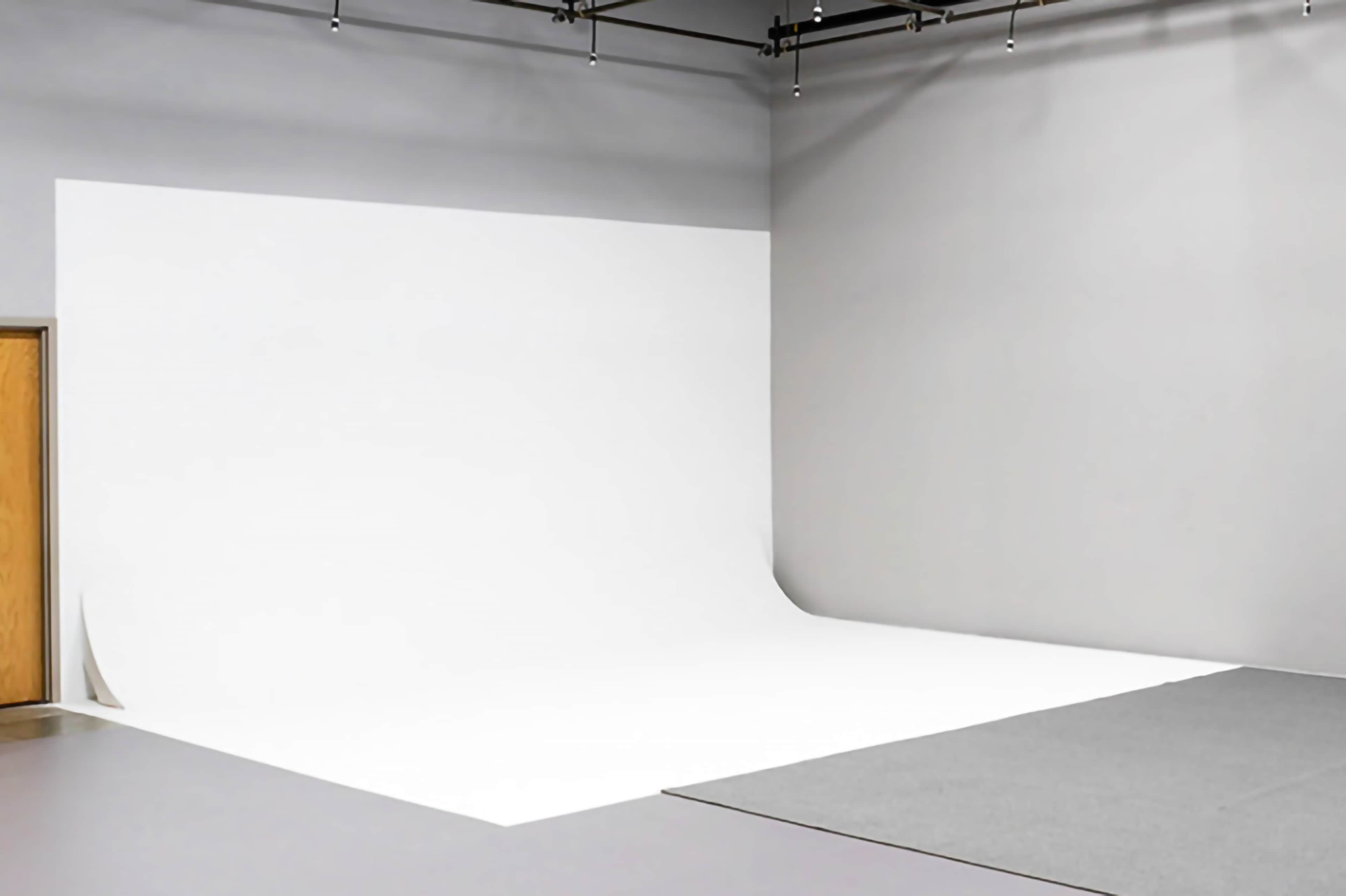 A photography studio with a seamless white backdrop and a gray floor.