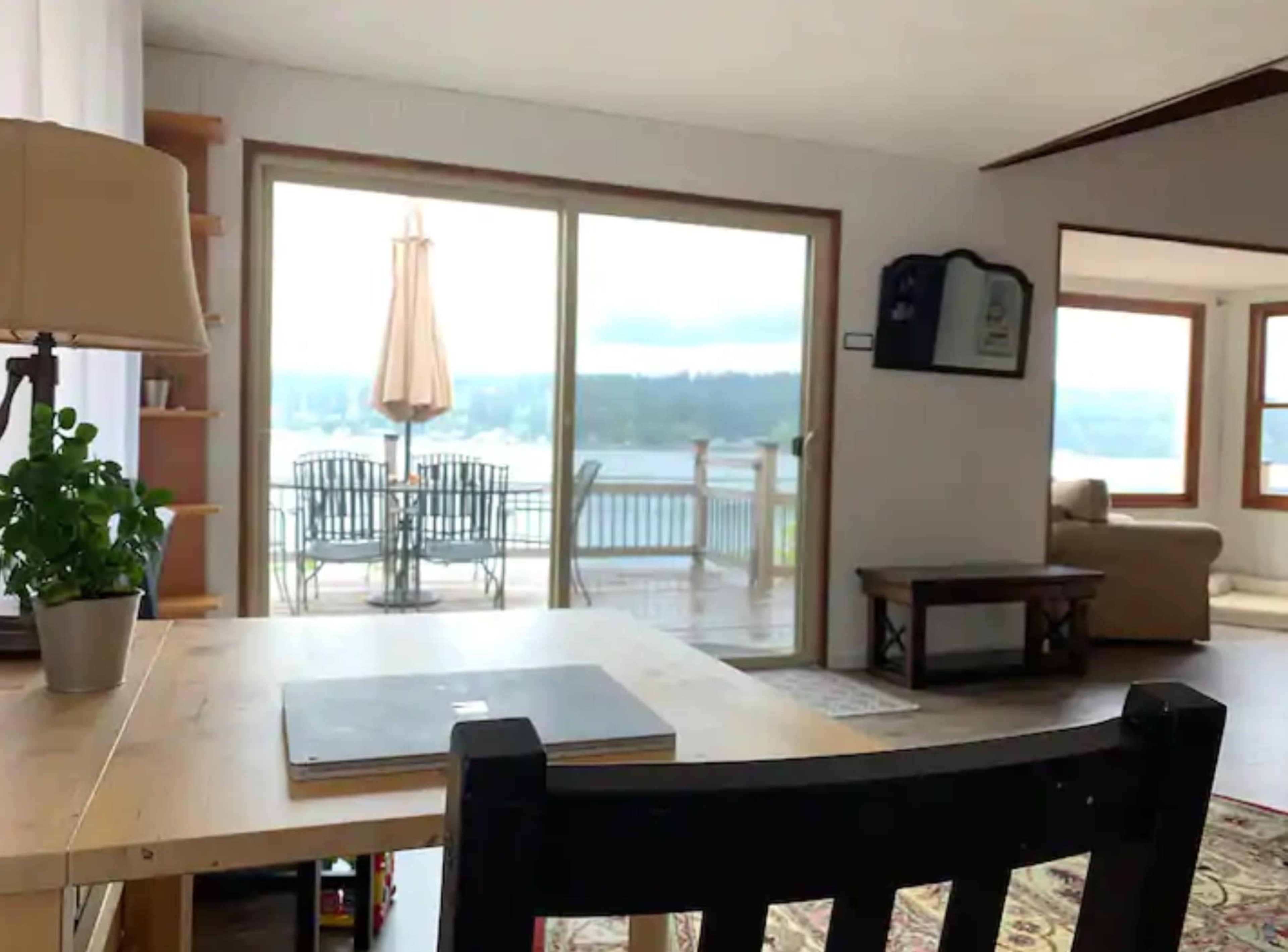 A cozy room with a wooden desk, a chair, and a sliding glass door leading to a deck overlooking a body of water.