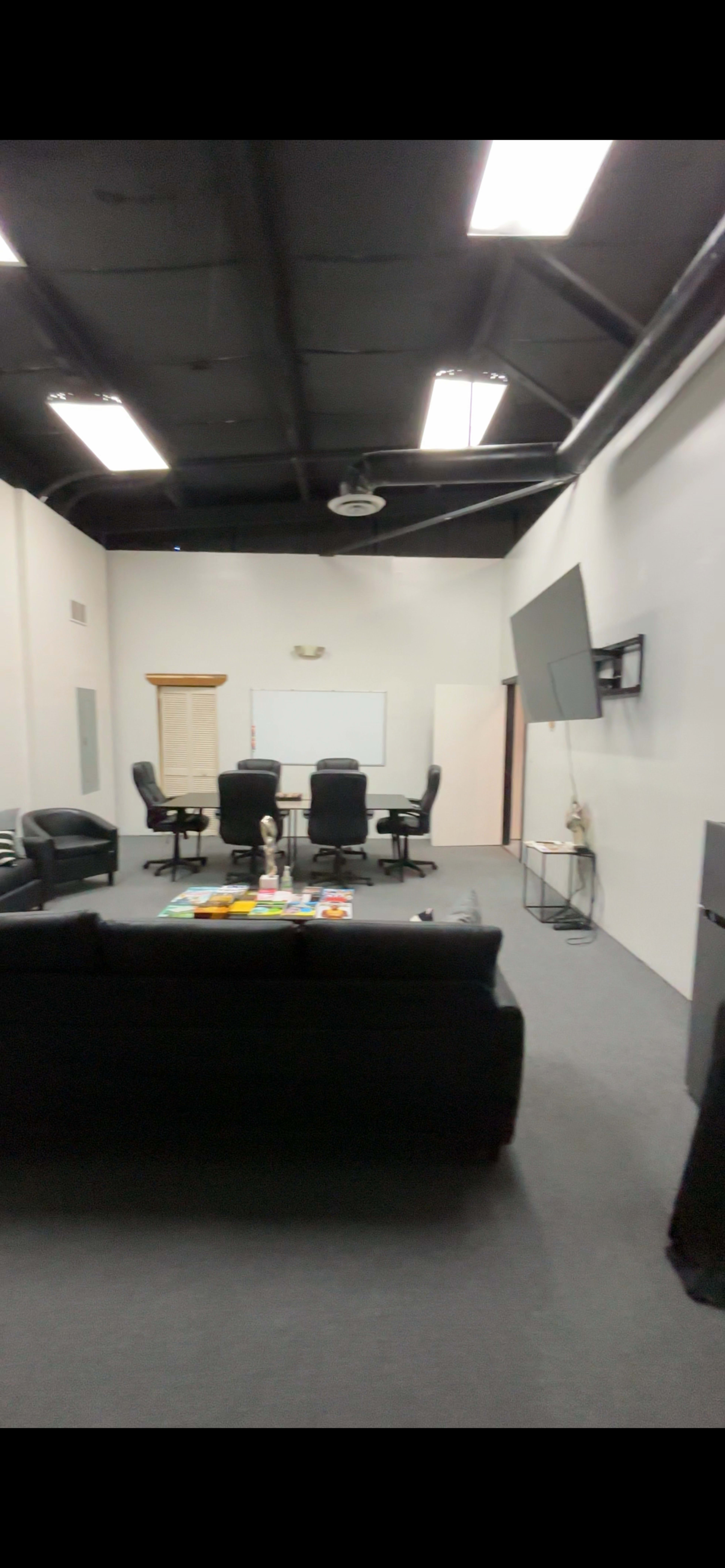 The image shows a conference room with black chairs, a couch, a TV mounted on the wall, and a whiteboard.