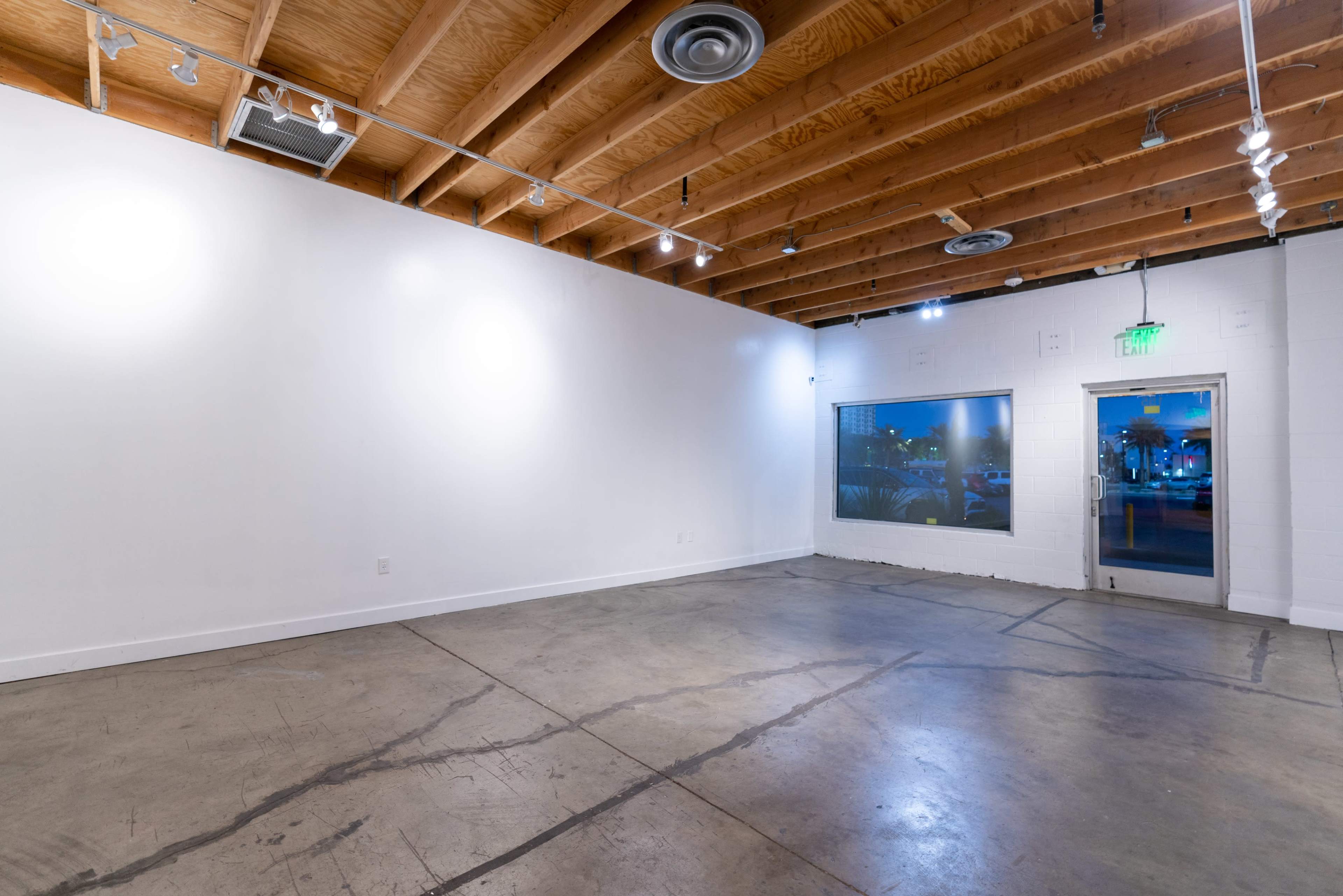 A spacious, empty interior with wooden beams and a concrete floor, featuring a window and an entrance door on one side.