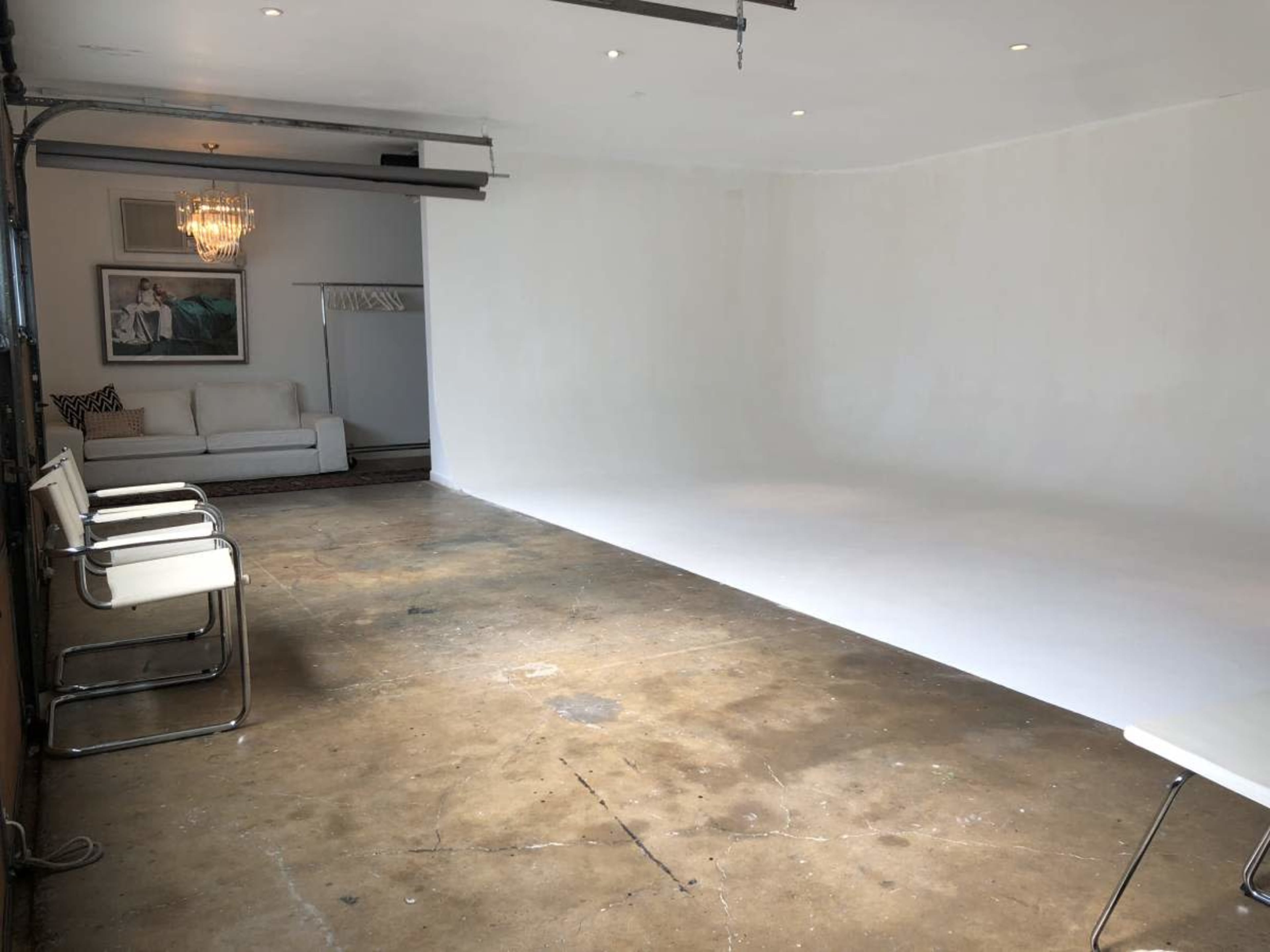 The image shows a spacious, empty studio with a white wall, concrete flooring, and a couch at the far end.