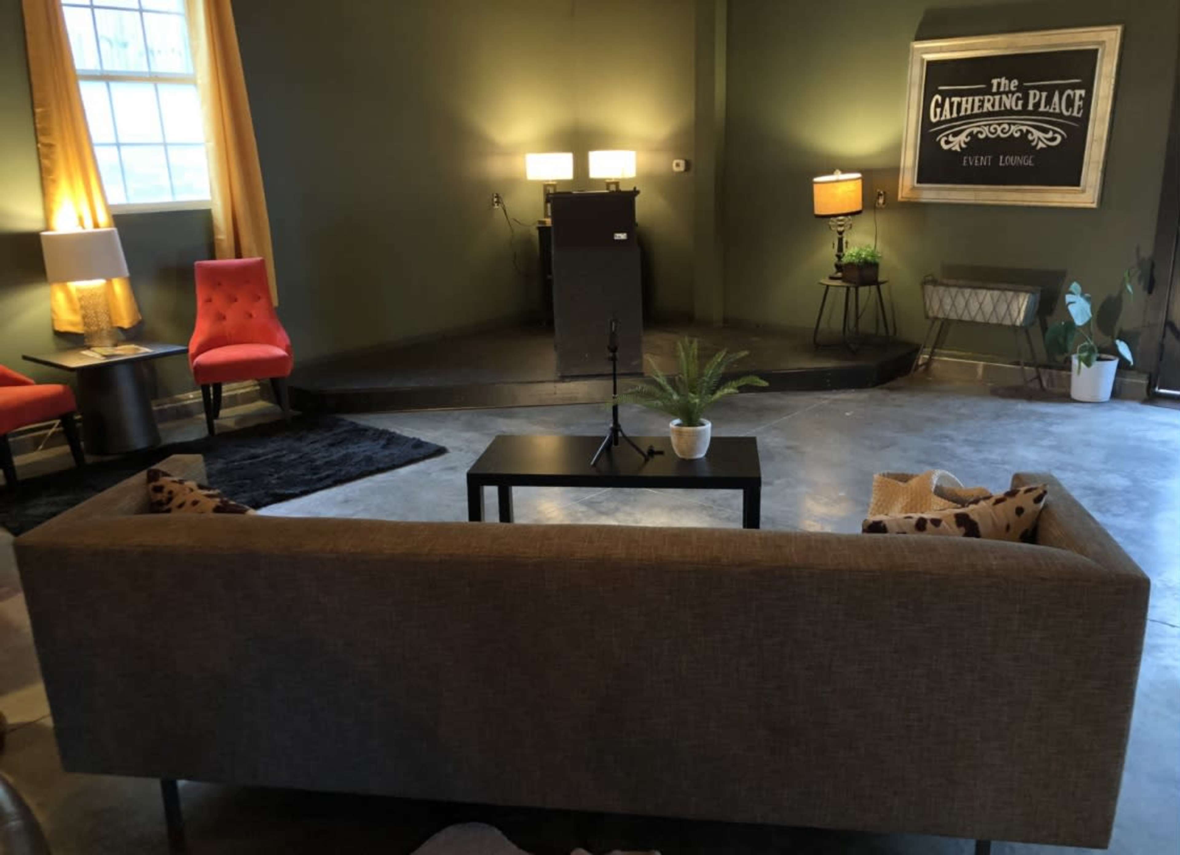 The image shows a cozy event space with a stage, seating areas, and decorative lighting.