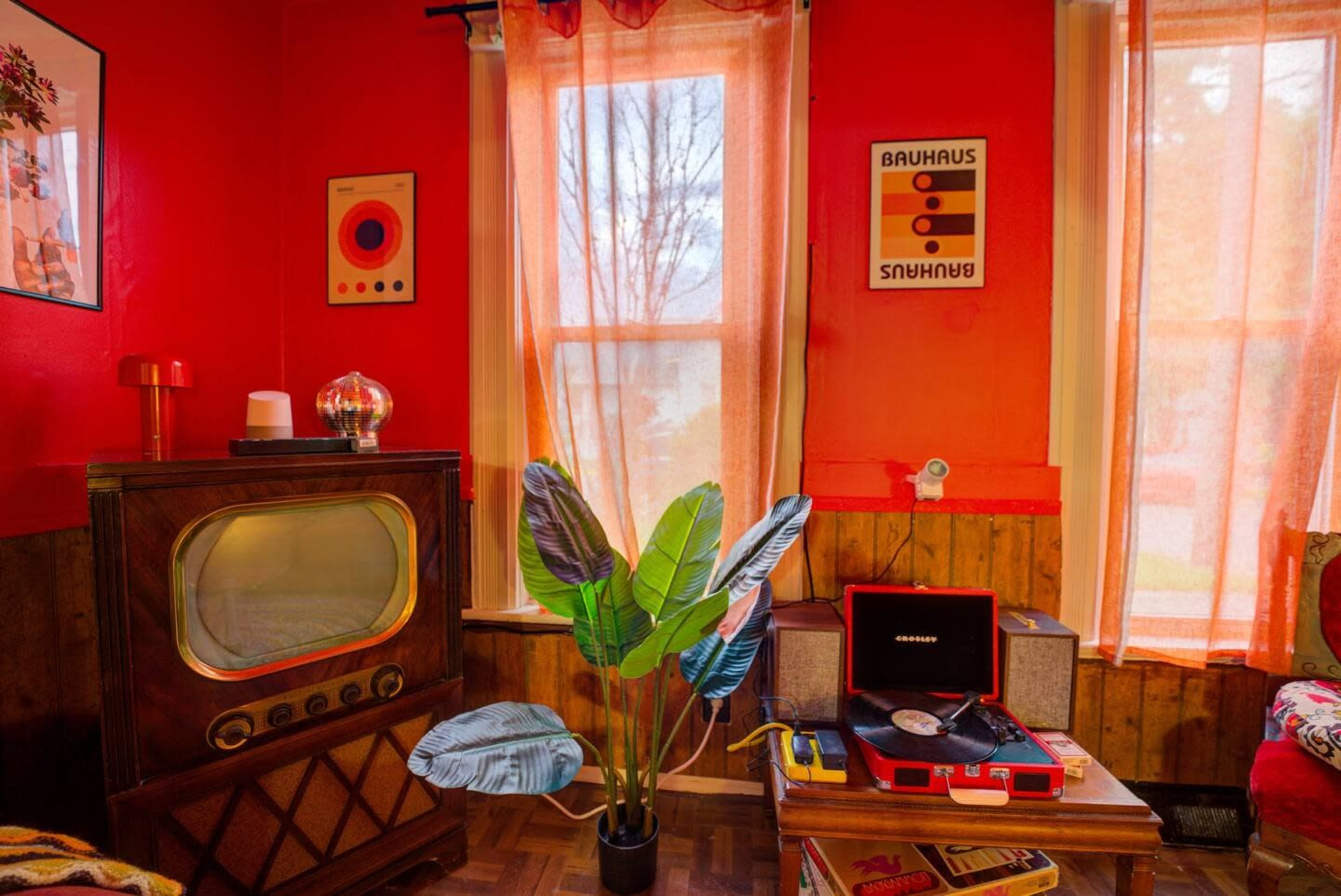A vintage living room with an old television, a record player, a potted plant, and bright red walls adorned with artwork.