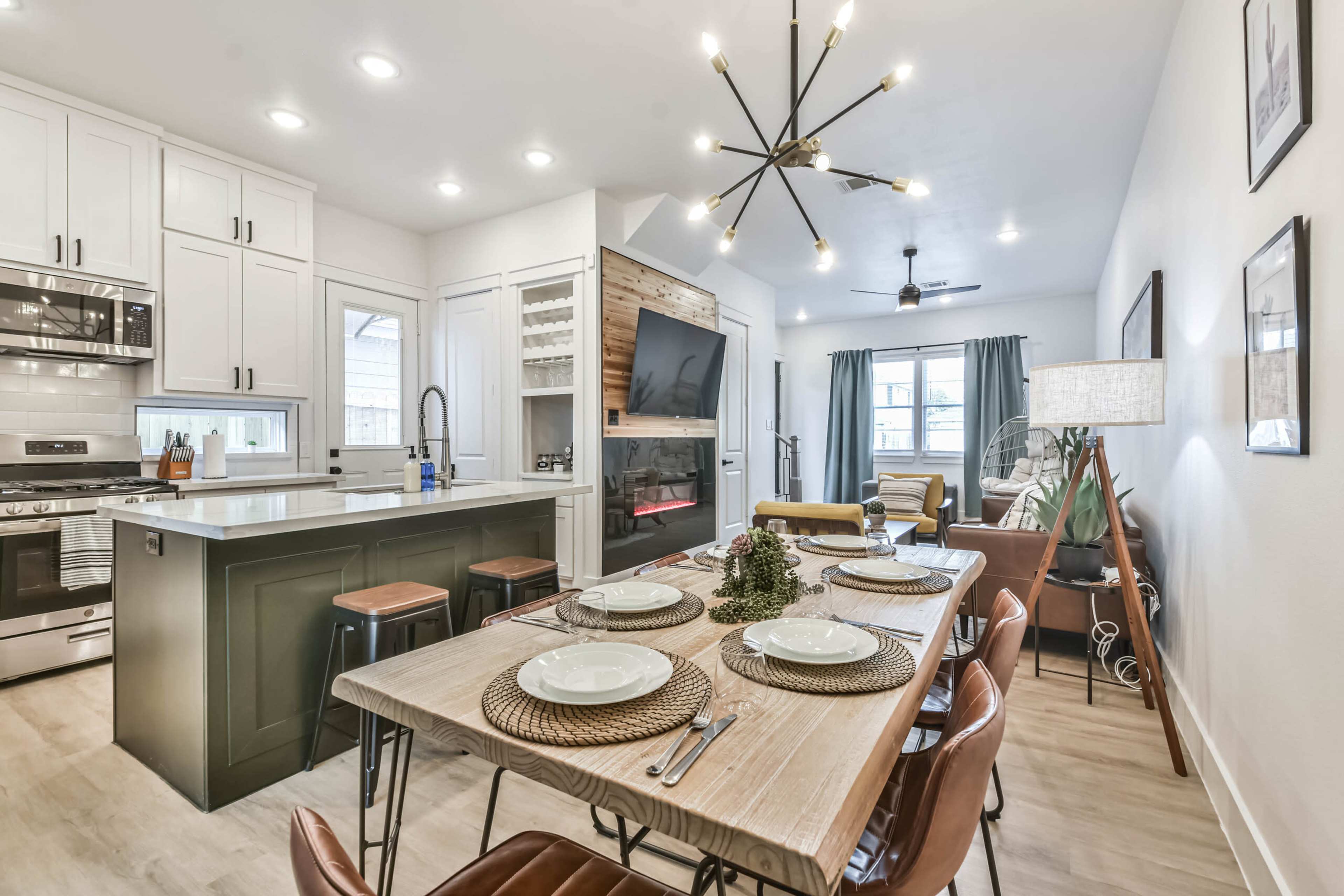 A modern kitchen and dining area with a table set for six, featuring a mix of sleek cabinetry, a central island, and a living space in the background.