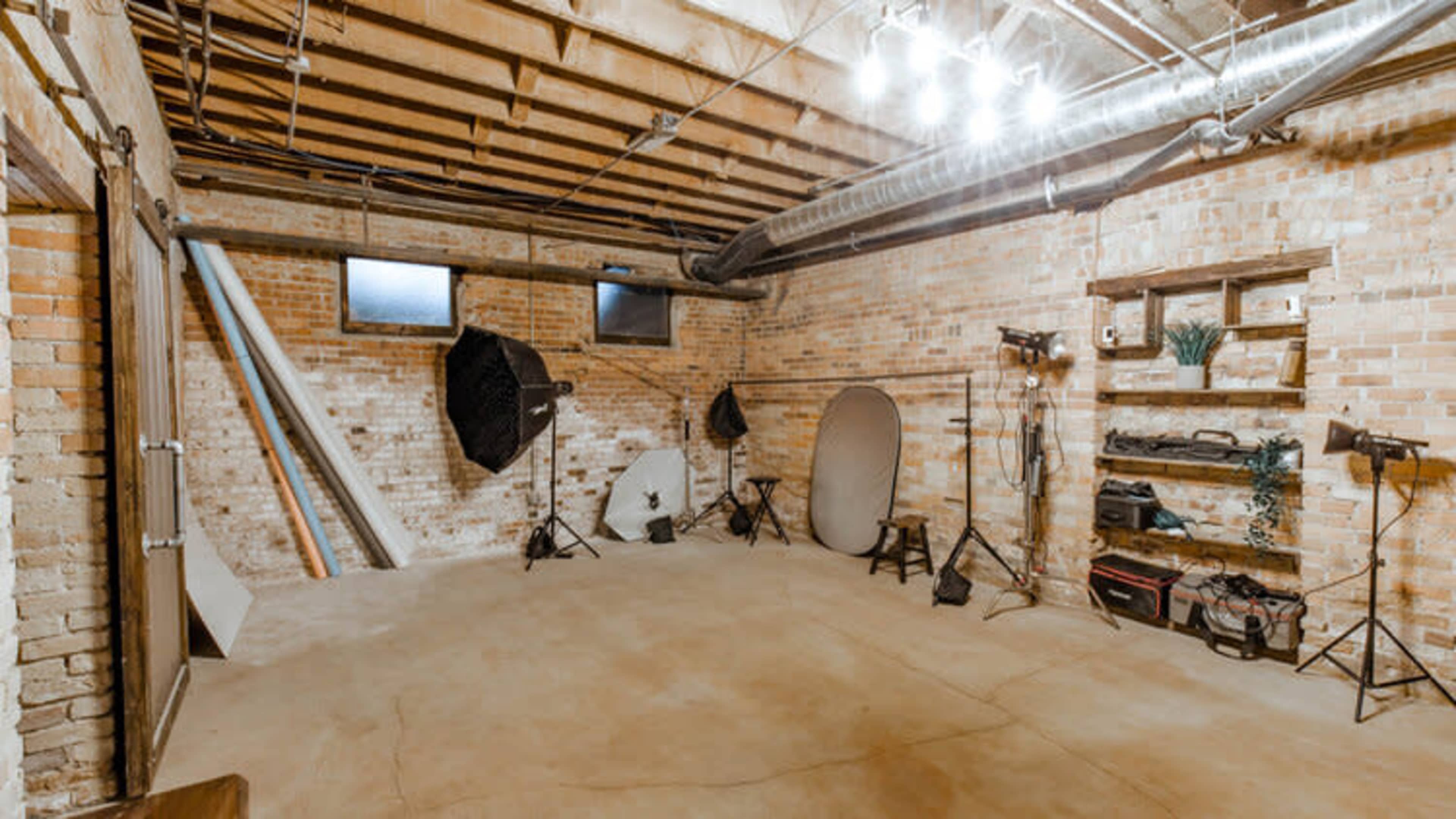 A spacious photo studio with exposed brick walls, featuring various lighting equipment and backdrops.