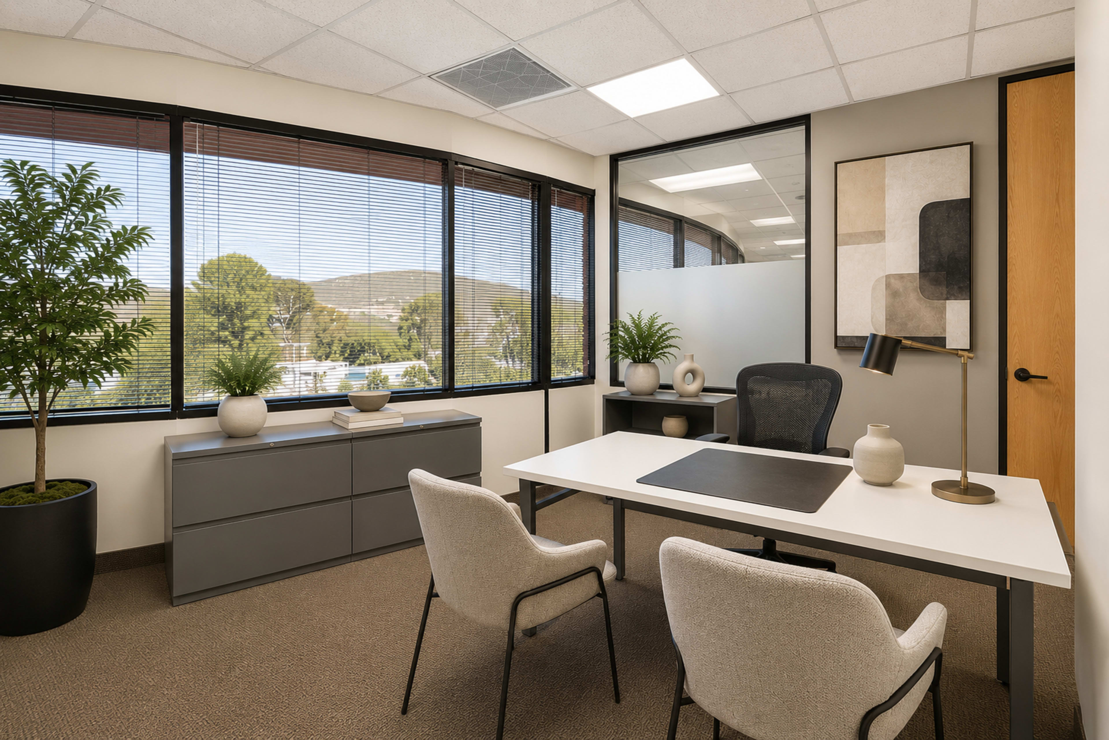 The image shows a modern office space with a desk, two chairs, and large windows offering views of greenery and hills.