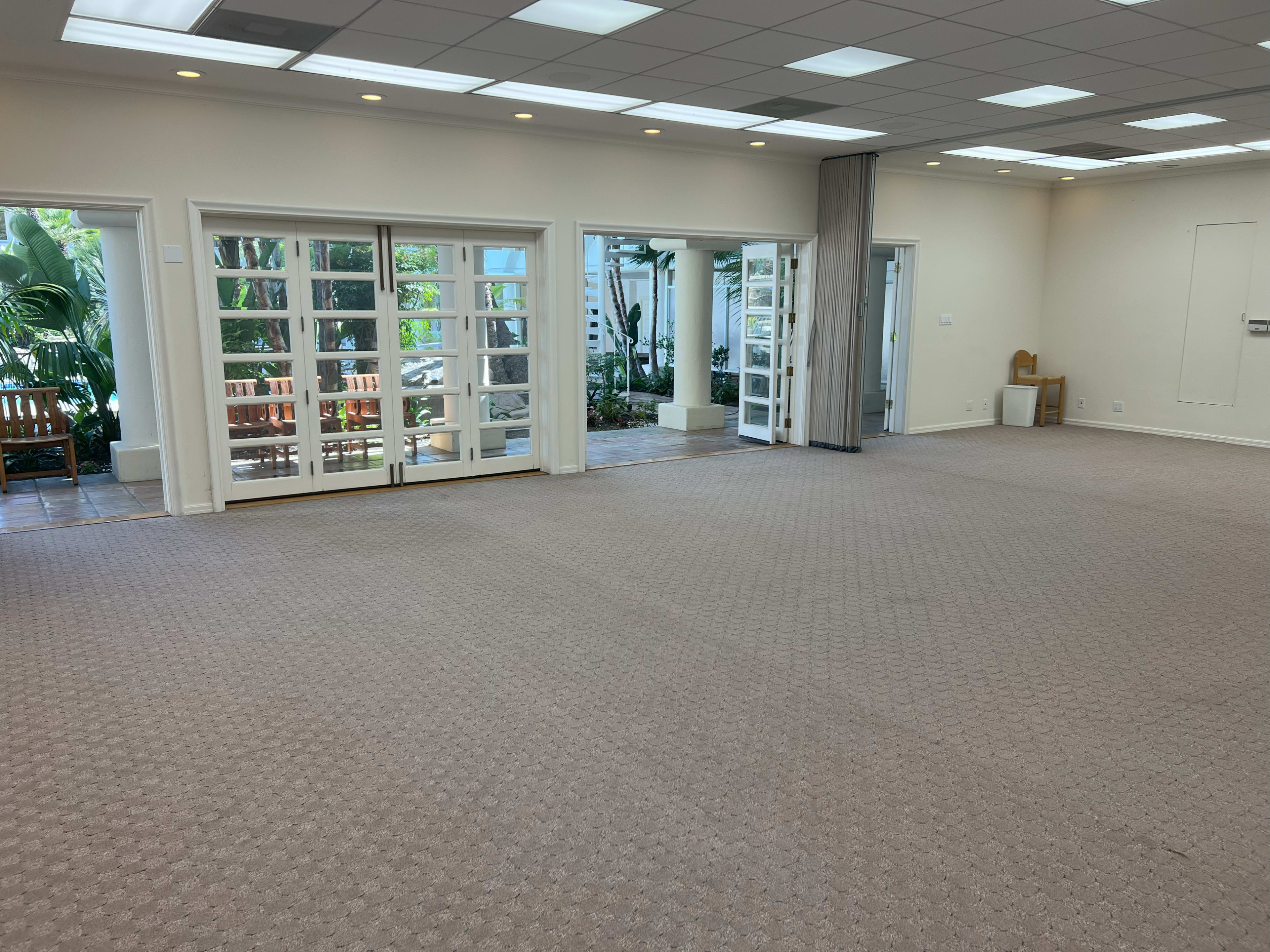 A spacious, empty room with beige carpet and multiple glass doors leading to an outdoor area.