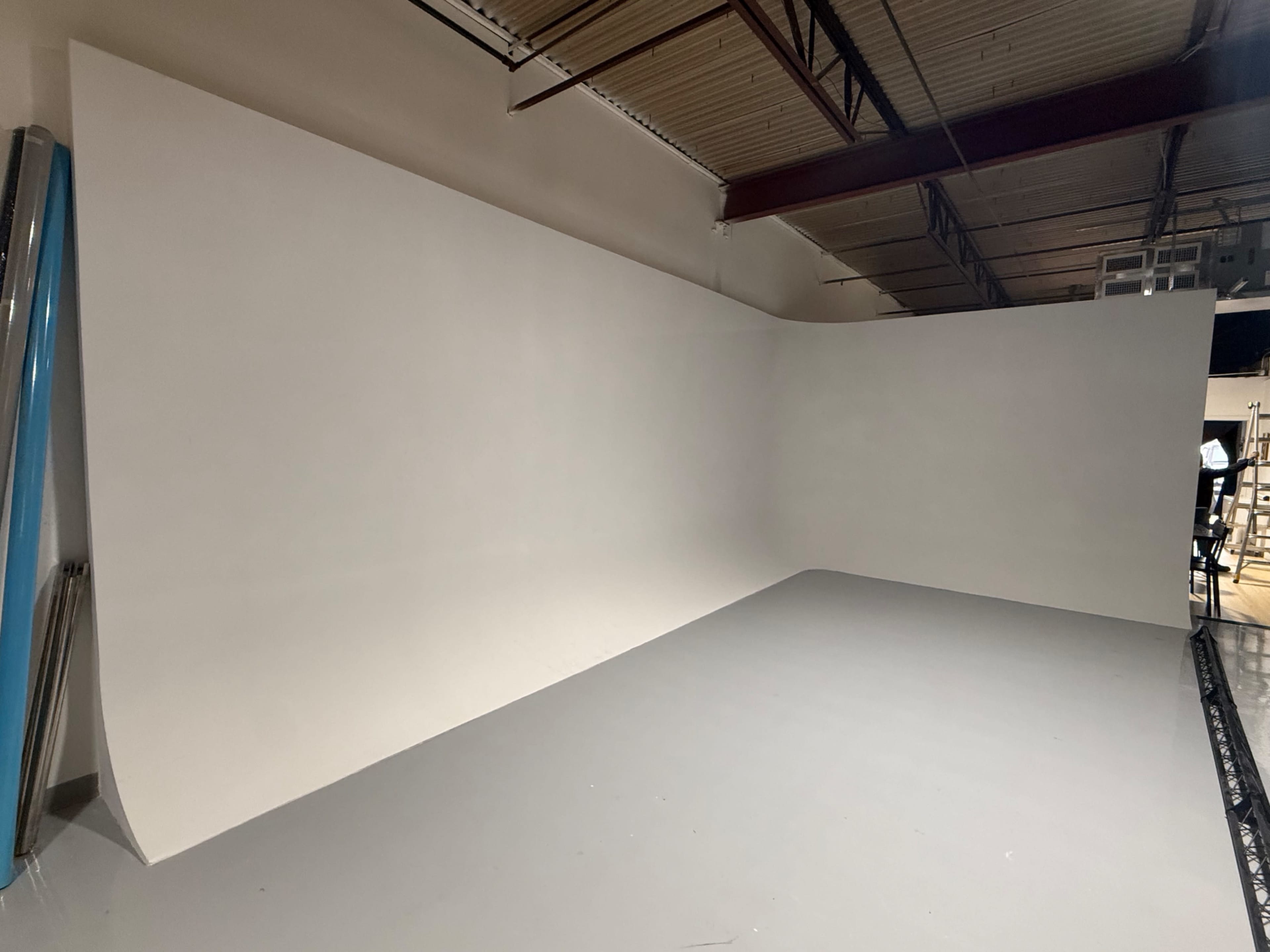 The image shows a spacious, empty studio with a seamless white background and gray flooring.