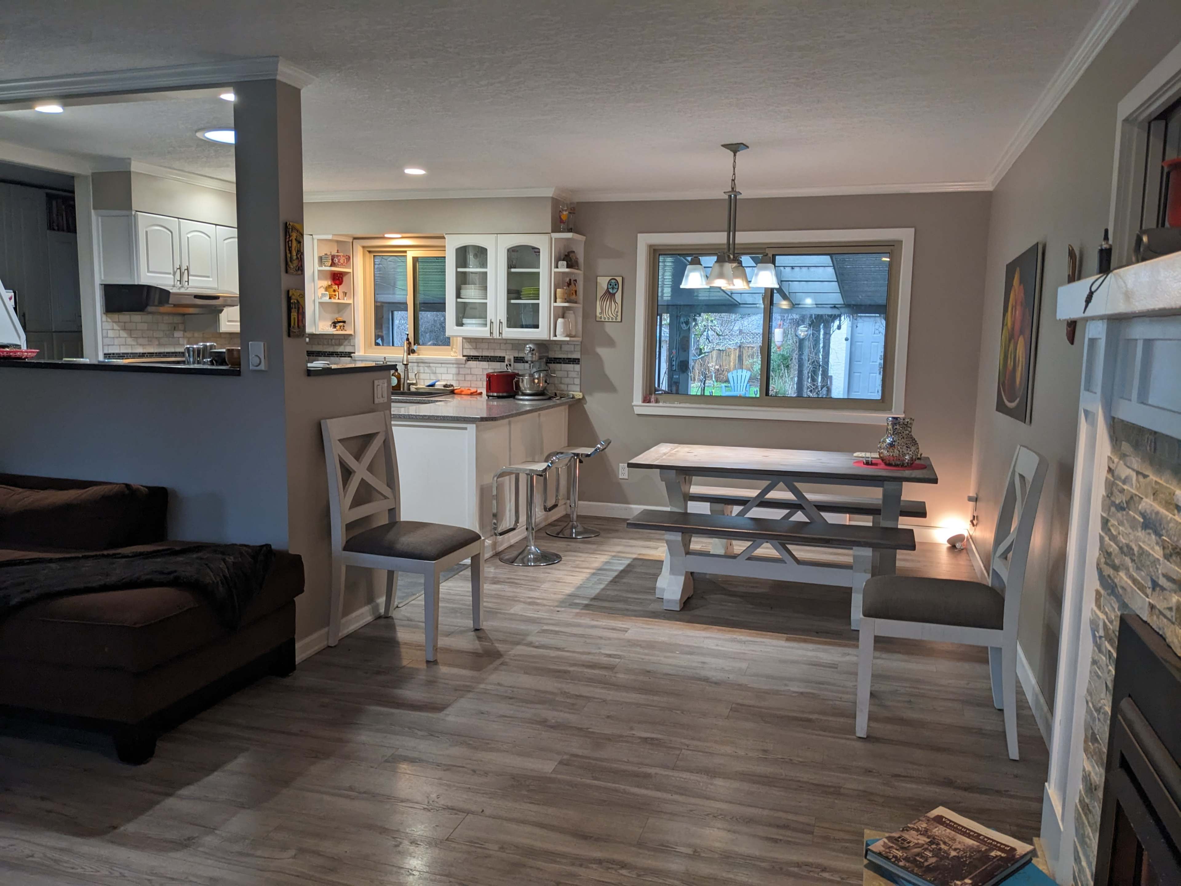 The image shows a modern, open-concept living space that includes a dining area with a table and chairs, a kitchen with white cabinetry, and a cozy seating area with a sofa.