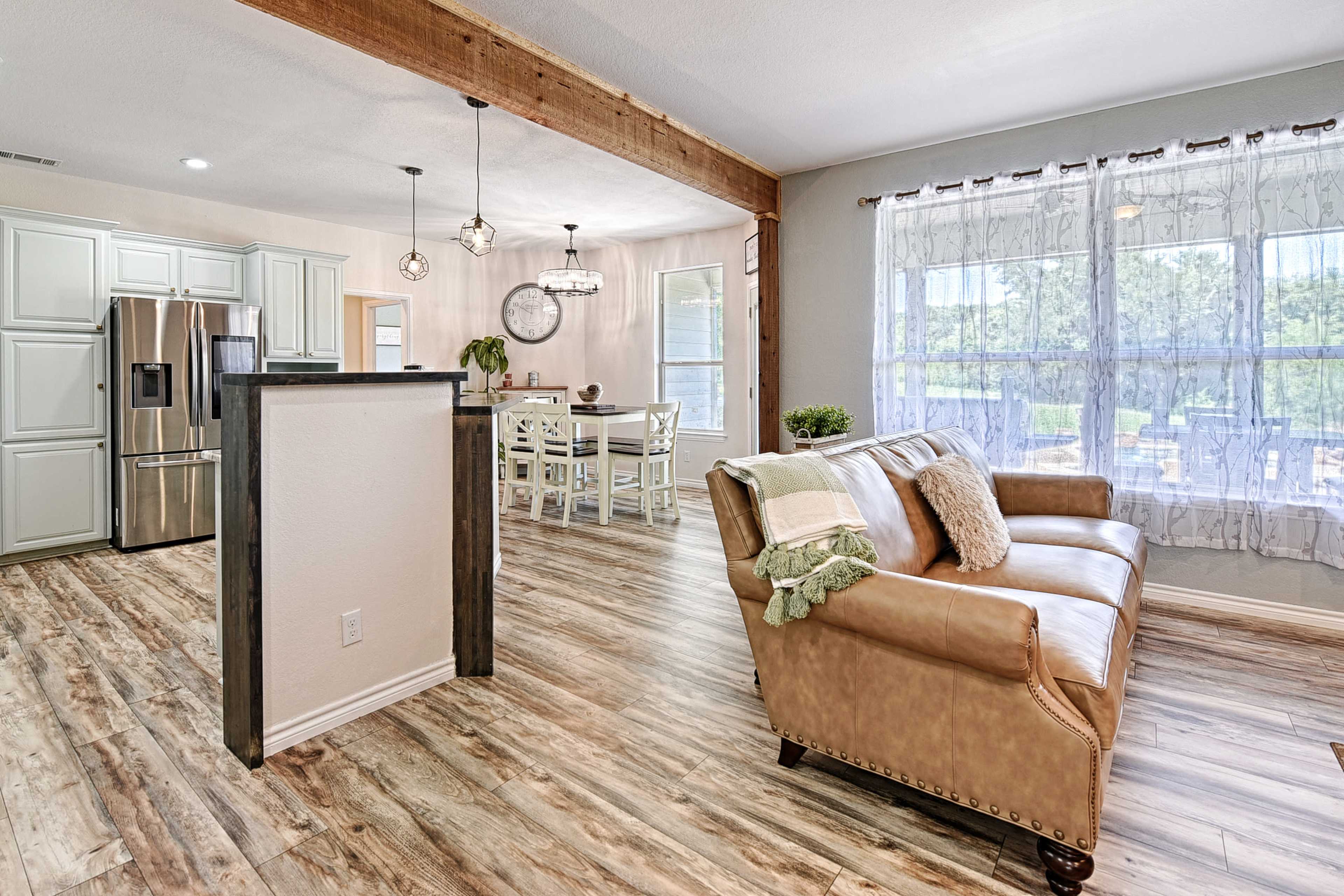 The image shows a modern, open-concept living area featuring a leather sofa, a dining table, and large windows that allow natural light to fill the space.