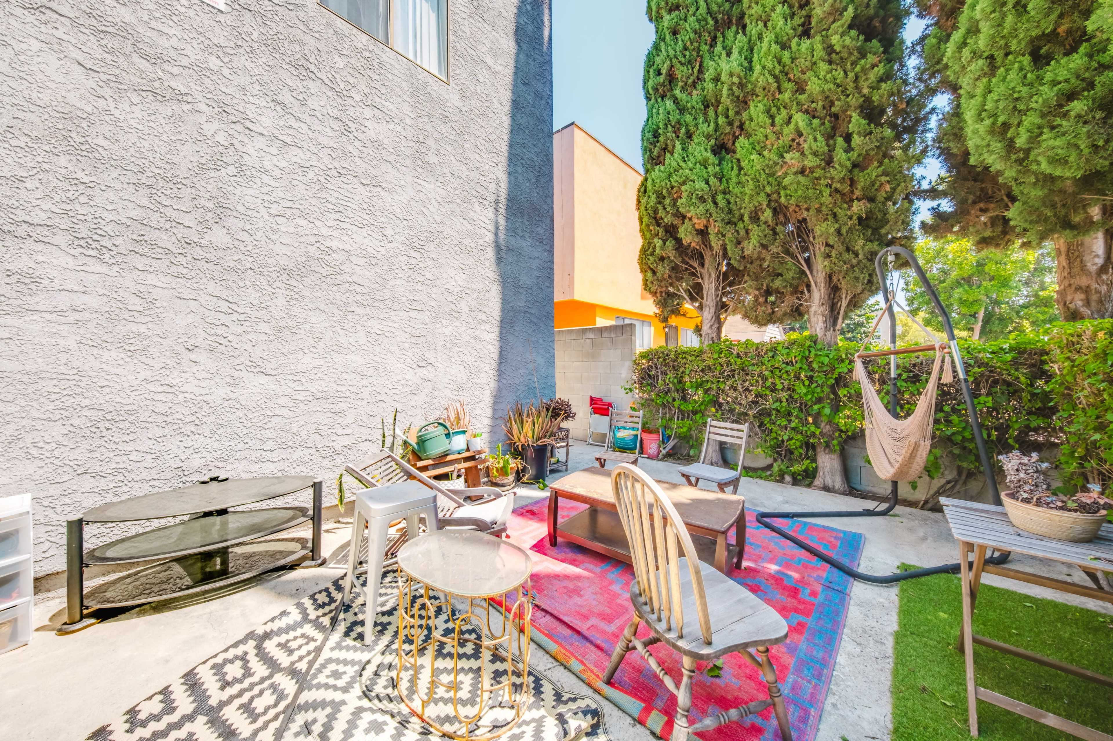 The image shows a small enclosed outdoor space featuring various seating options, rugs, and greenery along the perimeter.