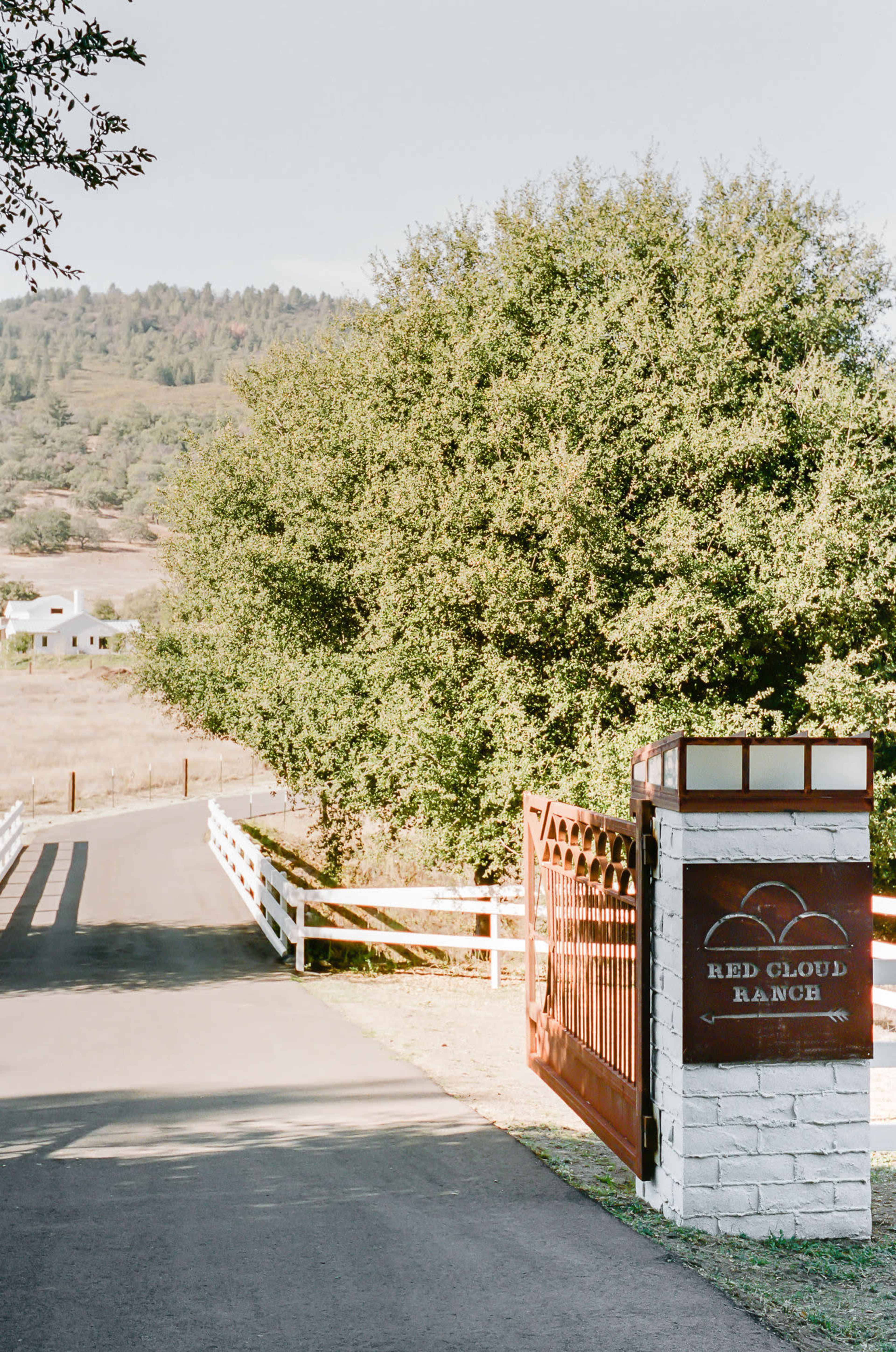 A gravel driveway leads to a gated entrance marked "Red Cloud Ranch," with lush greenery on either side.