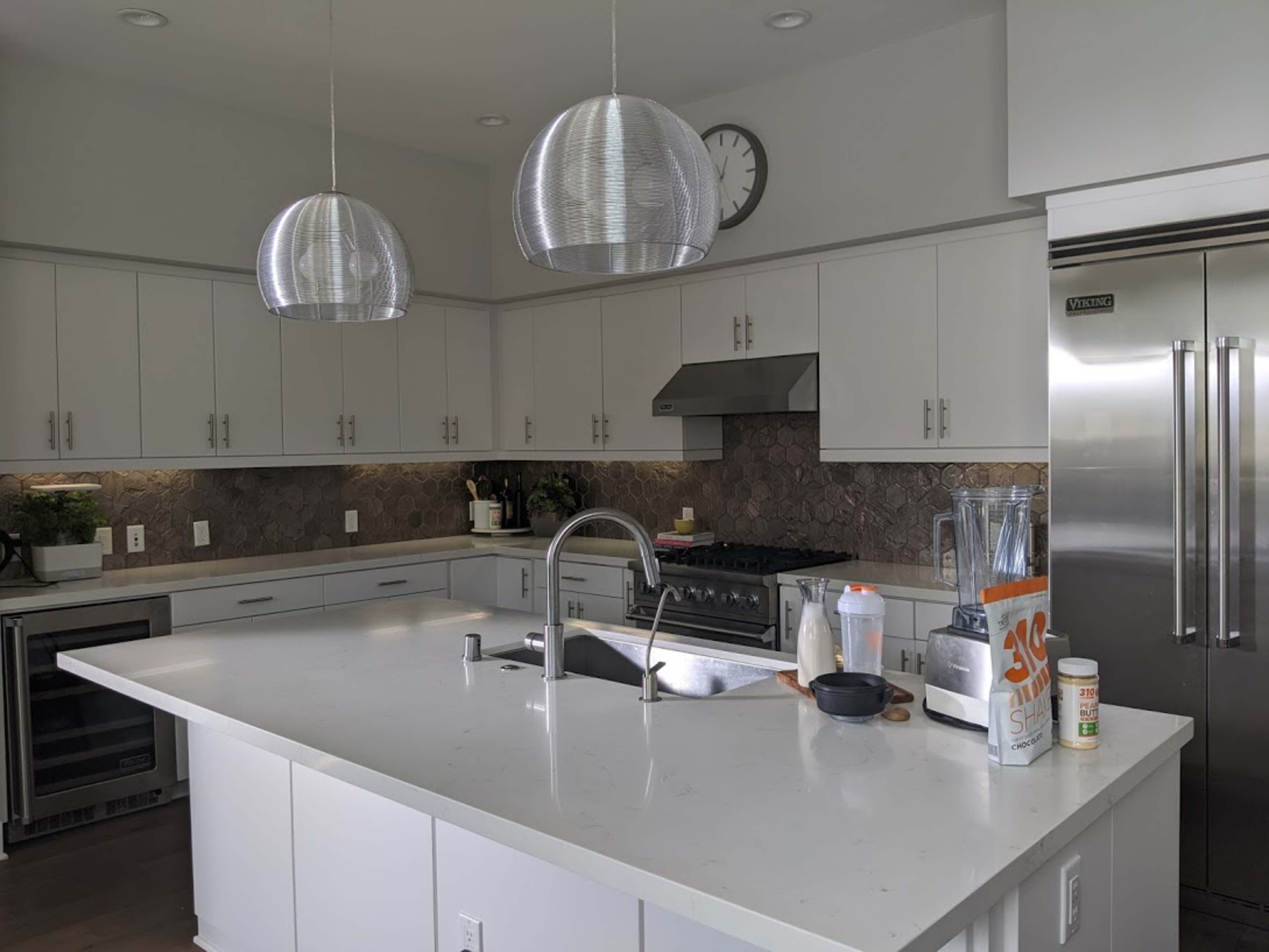 A modern kitchen features a large island with a sink, stainless steel appliances, and pendant lighting.