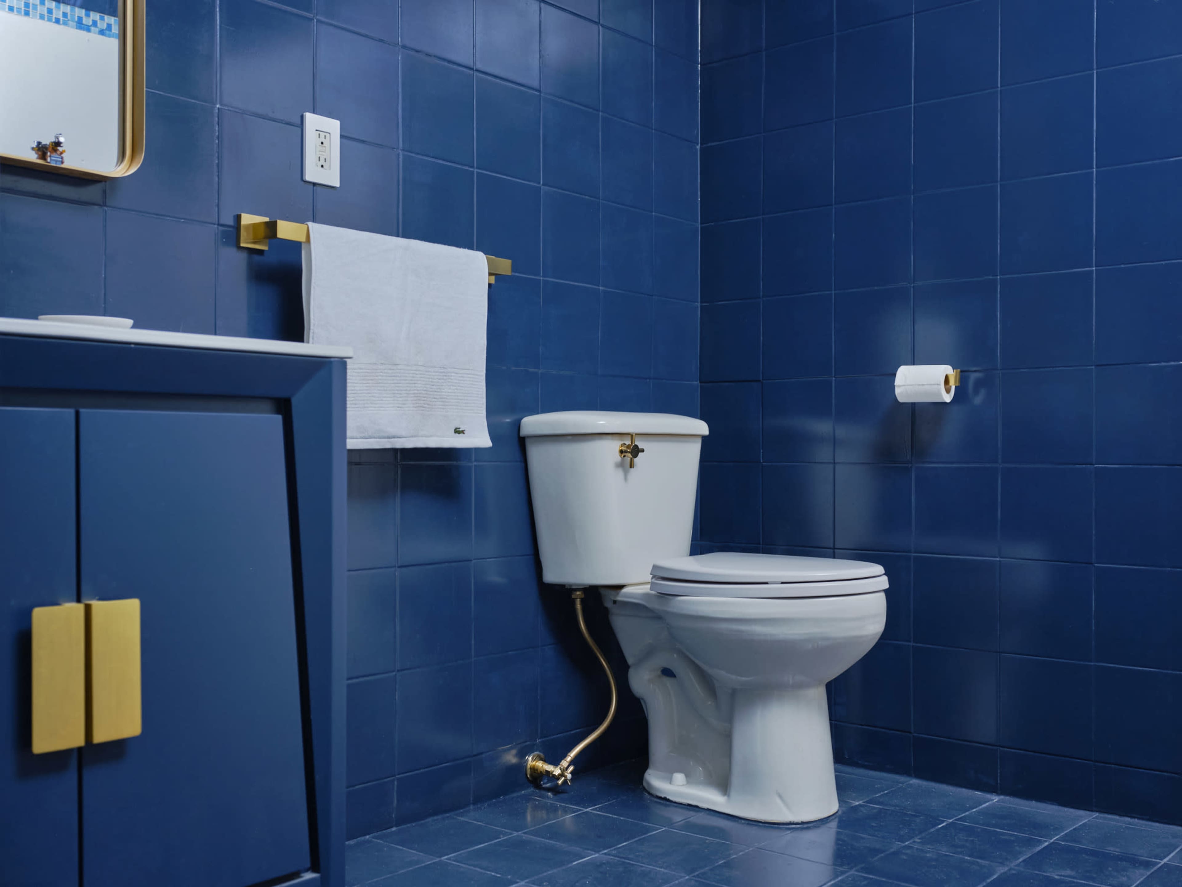 A bathroom featuring a white toilet, blue tiled walls, and a matching blue cabinet with gold accents.