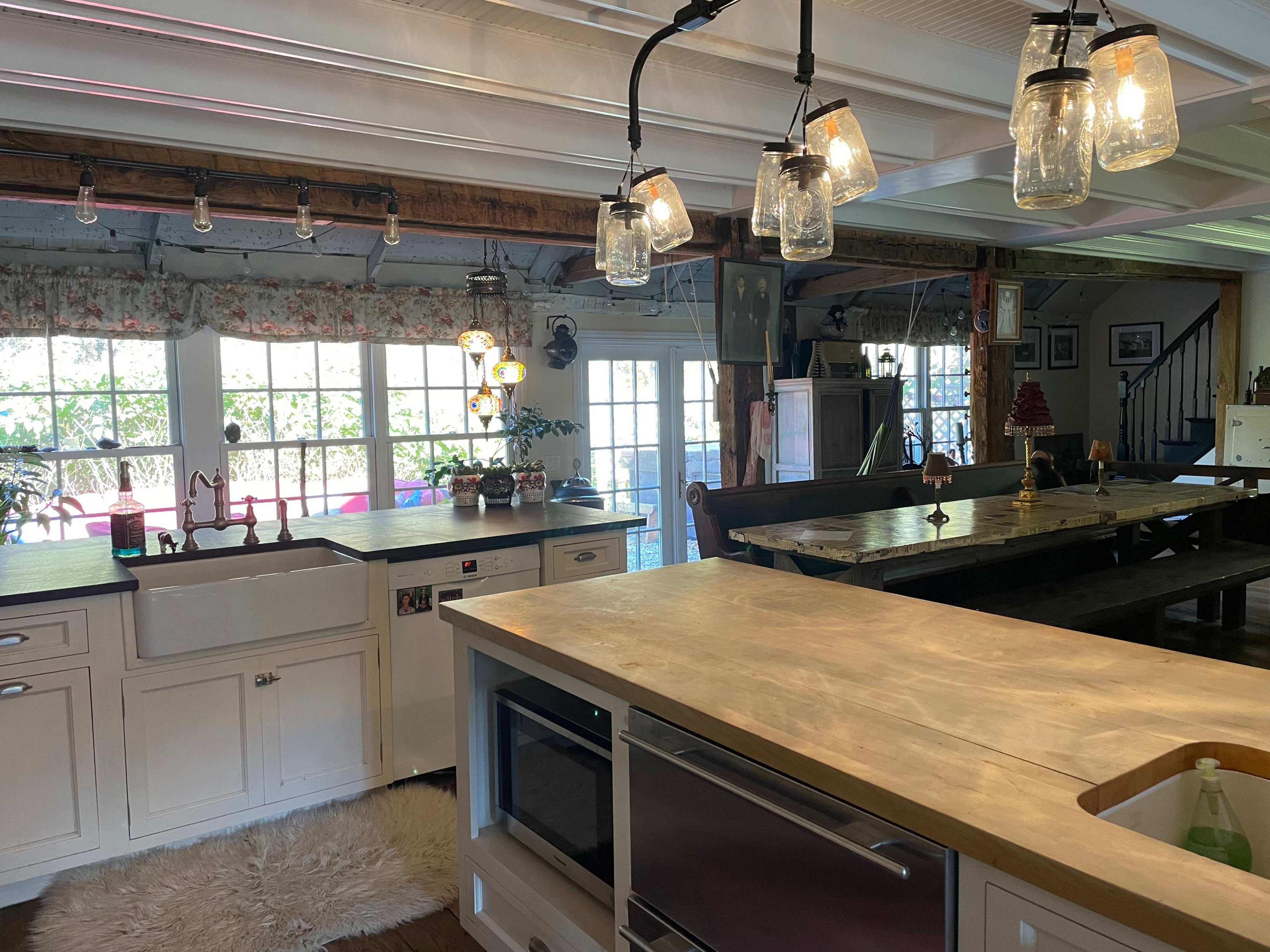 A spacious kitchen with white cabinetry, a large wooden table, and pendant lighting made from glass jars.