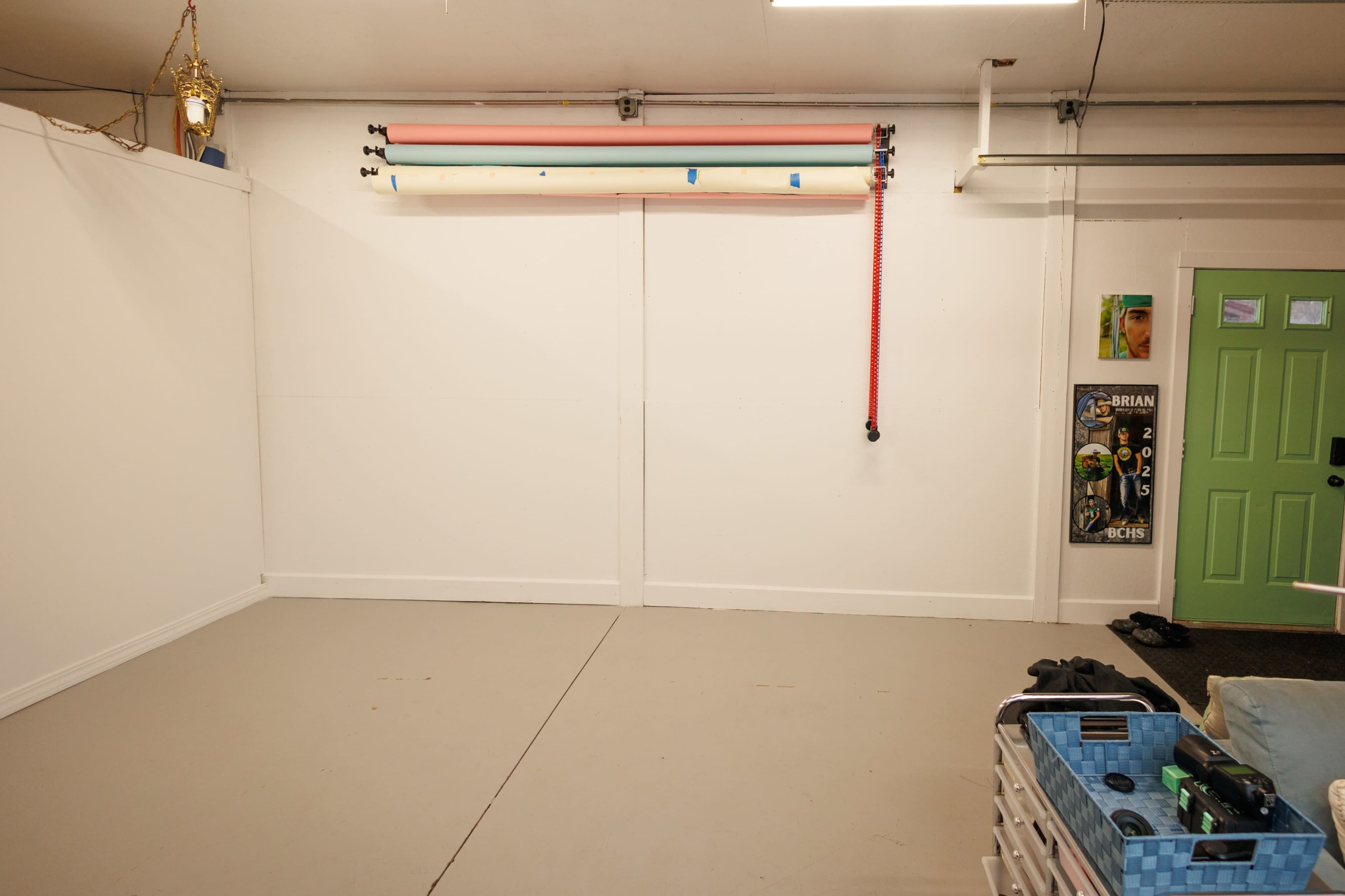 The image shows an empty room with a grey floor, white walls, and a green door, featuring several colored poles mounted on the wall above.