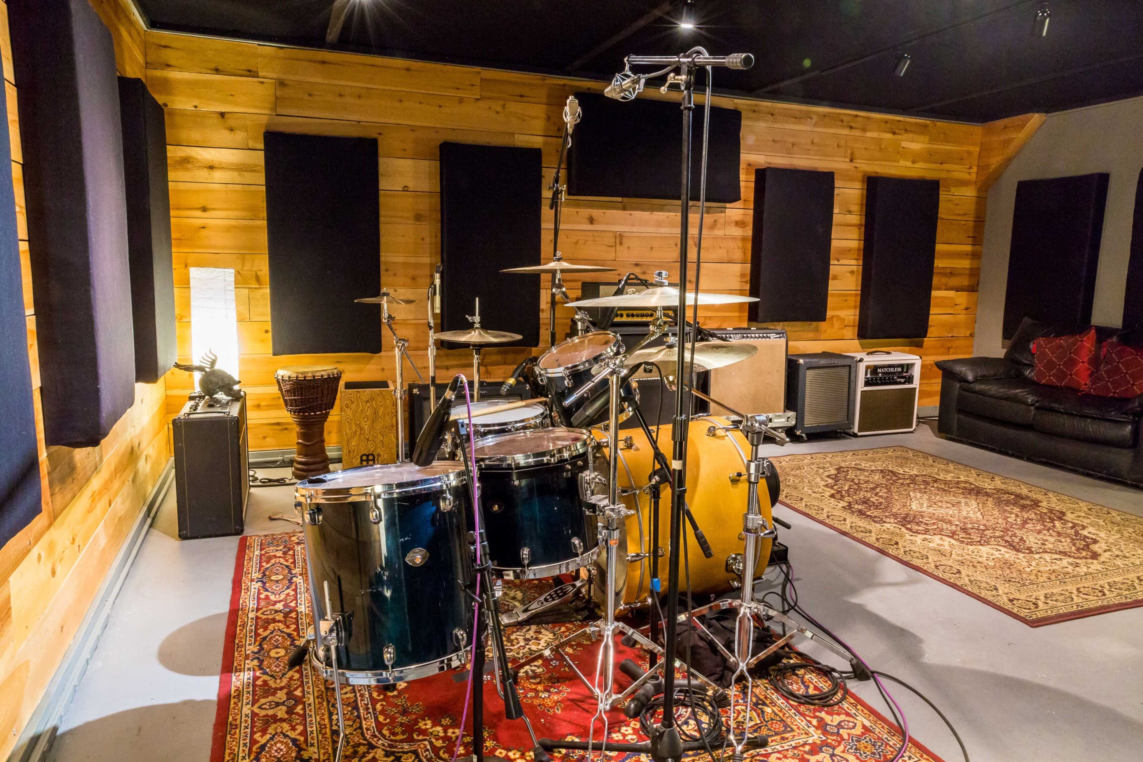 A drum set arranged in a recording studio with wooden walls, microphones, and various musical instruments in the background.