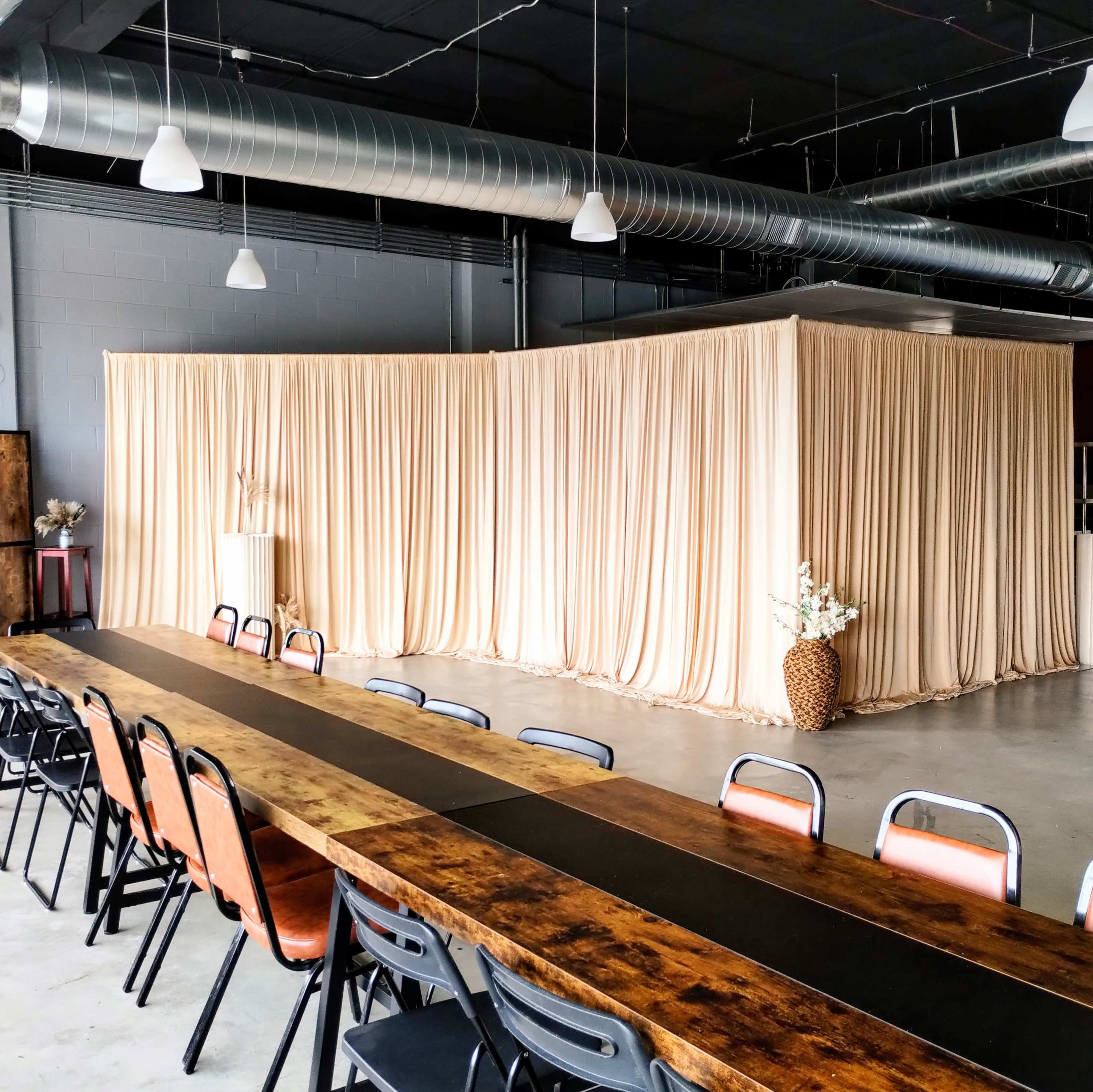 The image shows a spacious event room with a long wooden table and fabric drapes arranged in a semicircle at the far end.