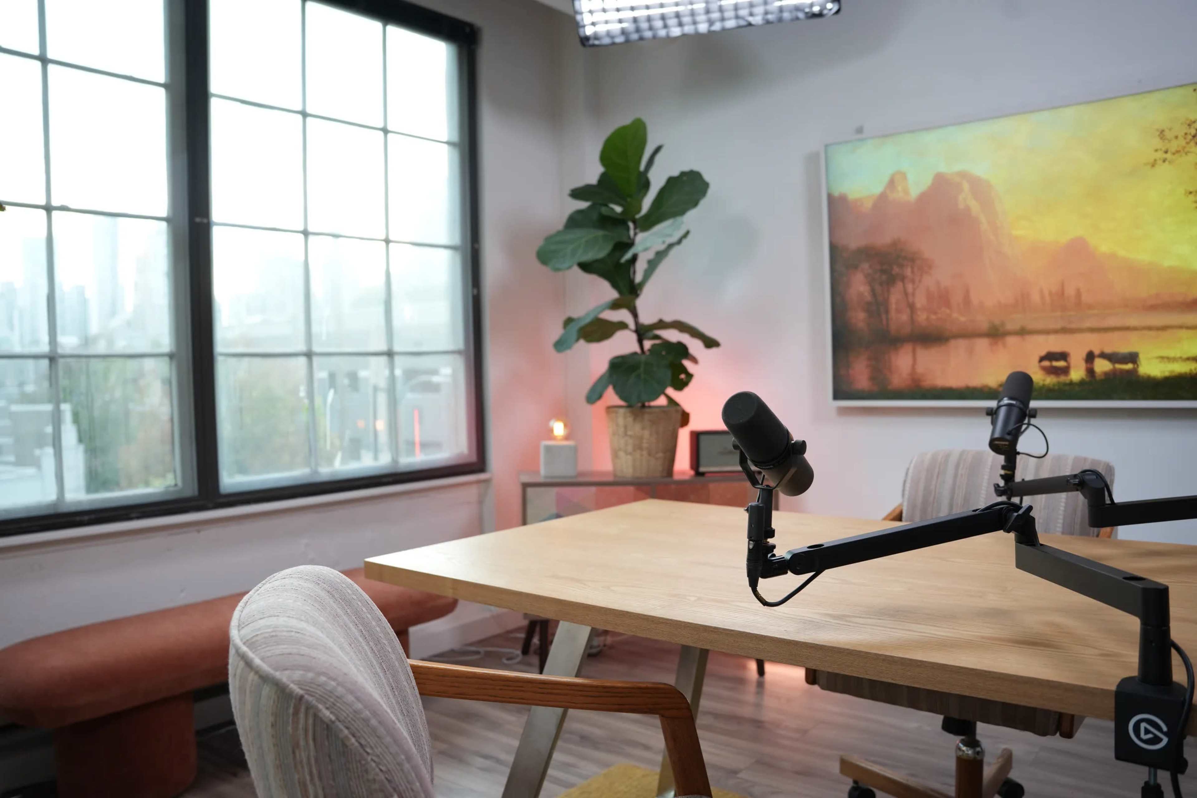 The image shows a modern office space featuring a wooden table, a microphone setup, a potted plant, and a large window displaying a foggy cityscape.