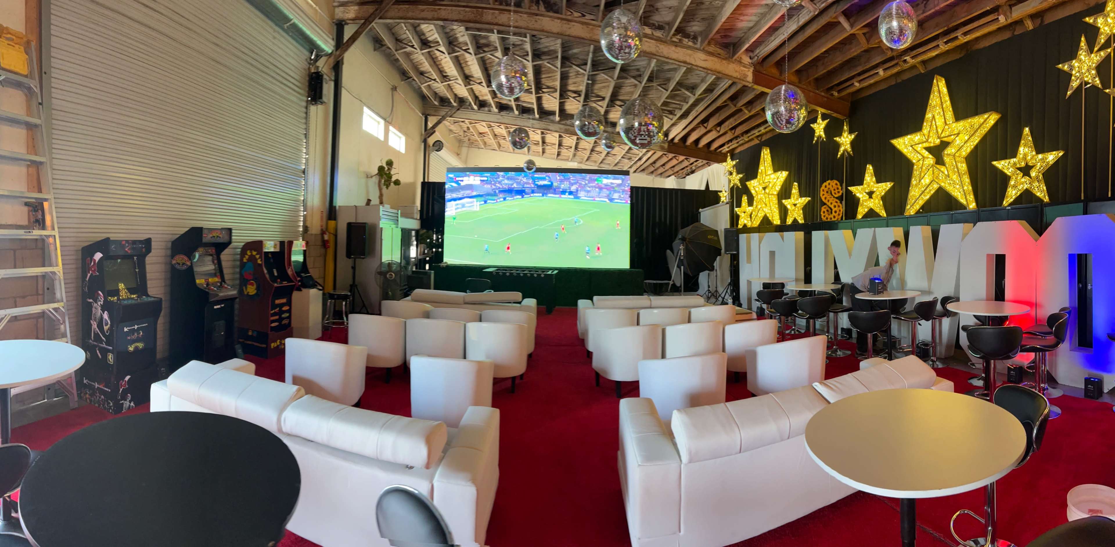 A spacious entertainment area features white seating, a large screen showing a sports event, and decorative stars on the walls.