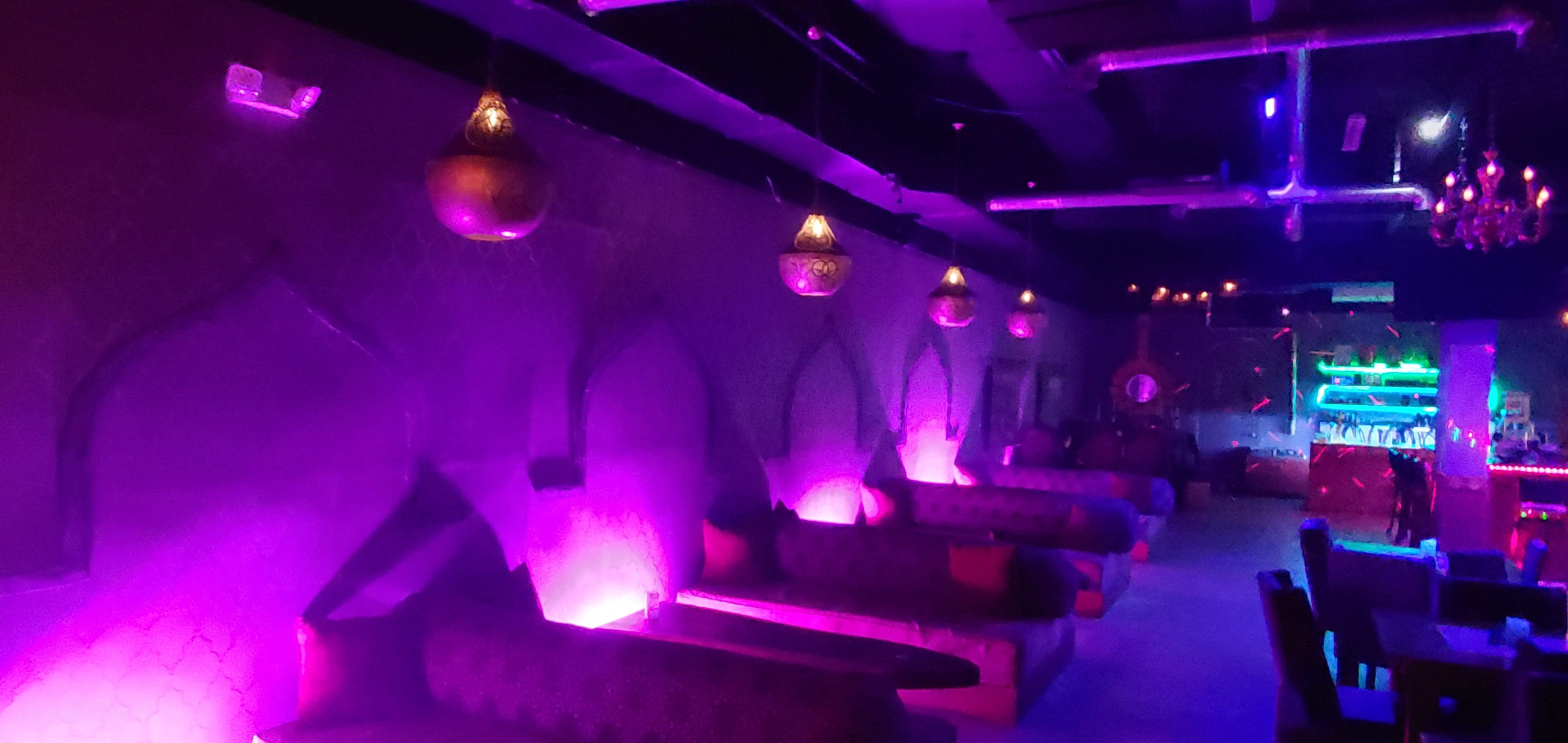 A dimly lit lounge features ornate seating, glowing purple lights, and decorative hanging lanterns along the walls.