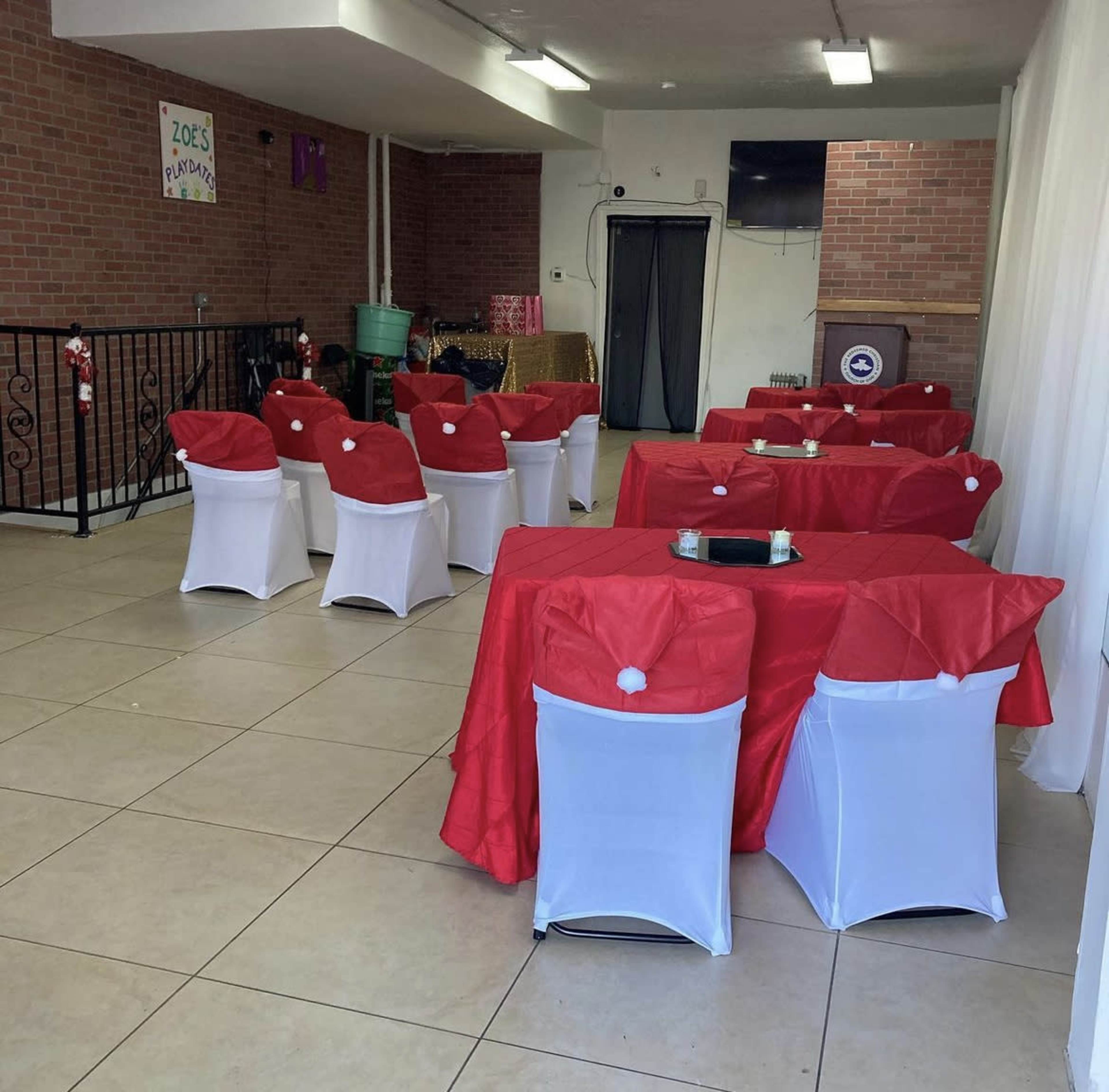 A decorated indoor space with tables covered in red tablecloths and white chair covers, arranged for an event.