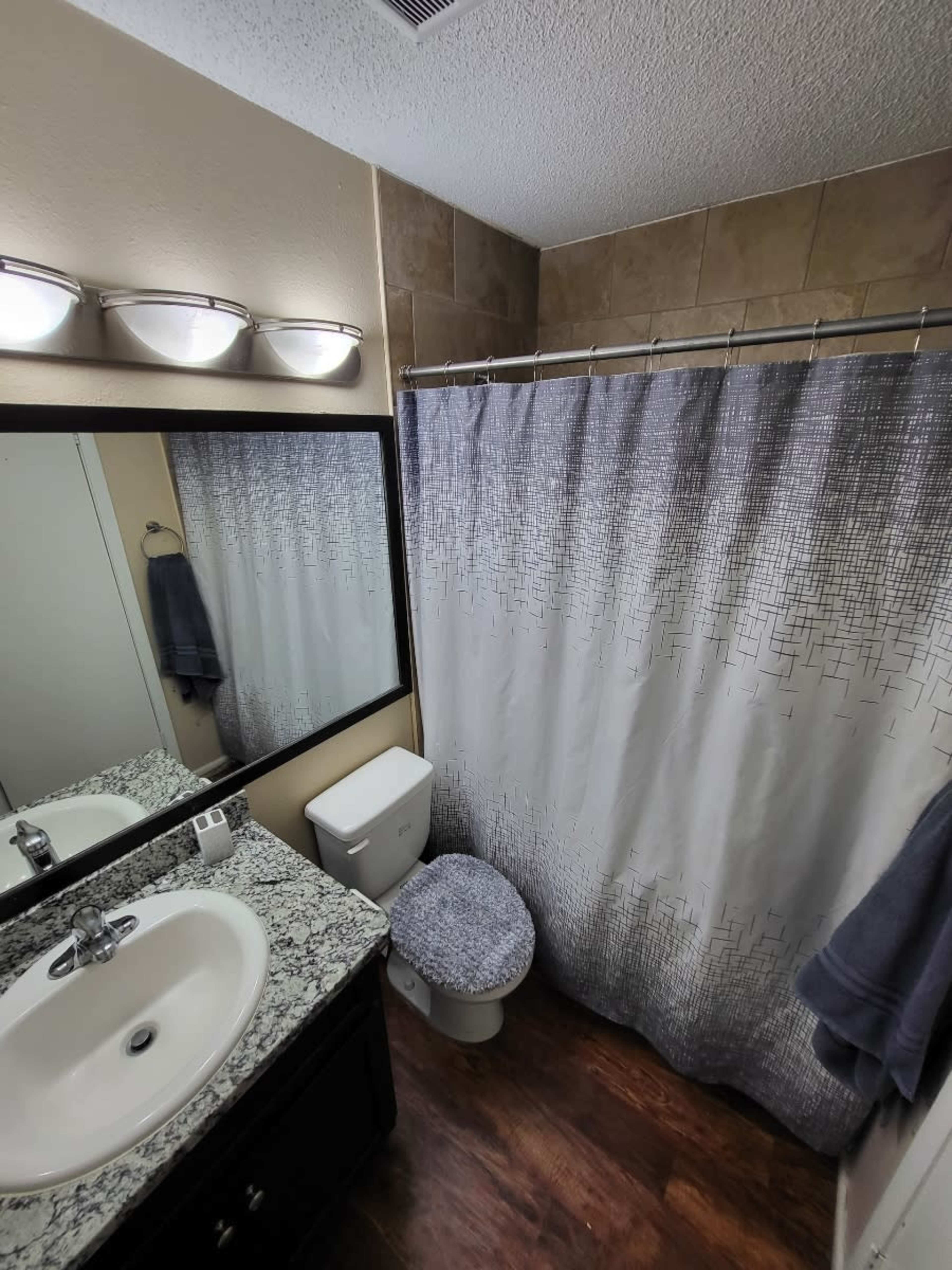 A compact bathroom featuring a sink with a mirror, a toilet, and a shower curtain over the bathtub.