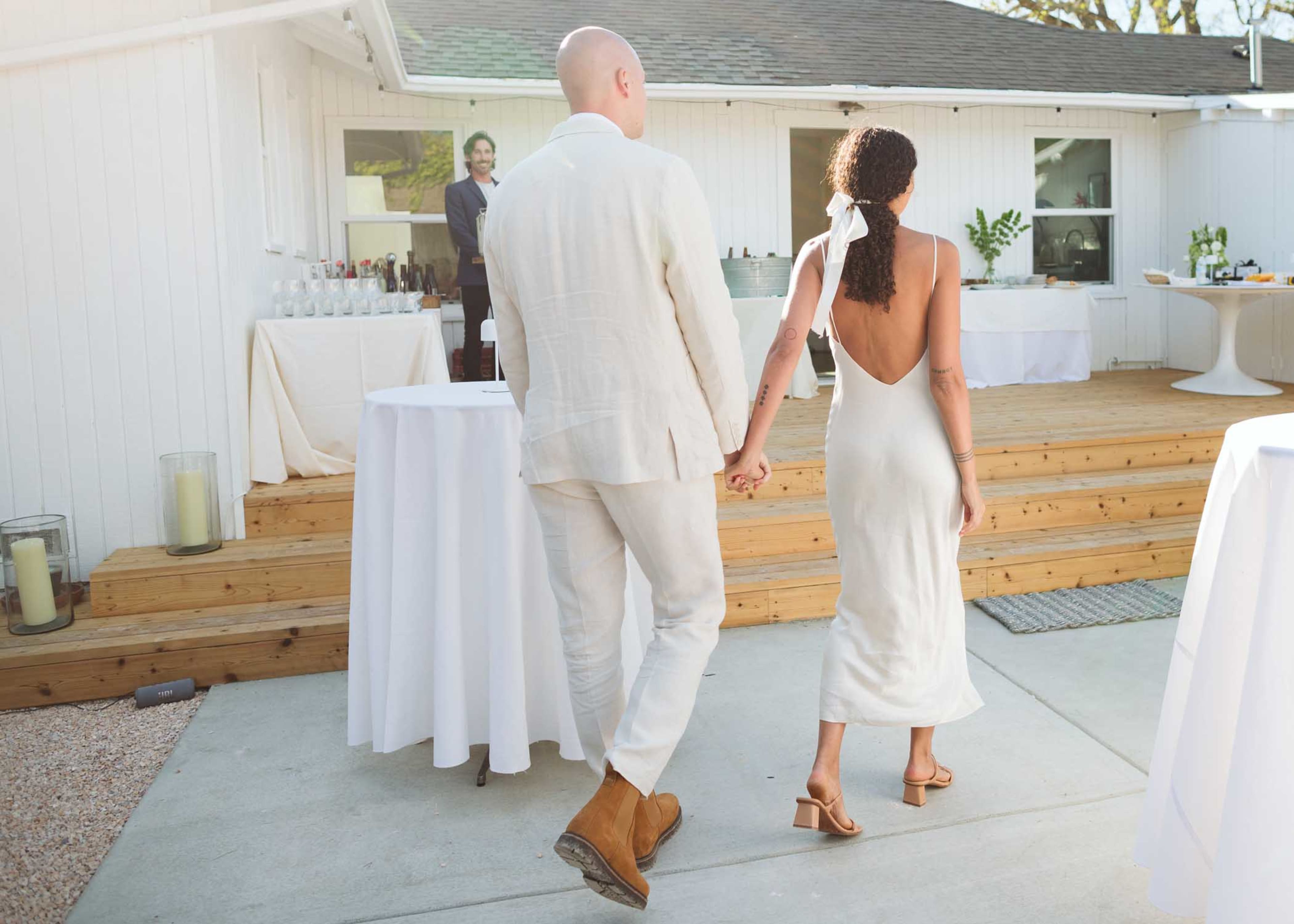 A couple walks hand-in-hand towards a reception area with tables and decorations set up for an event.