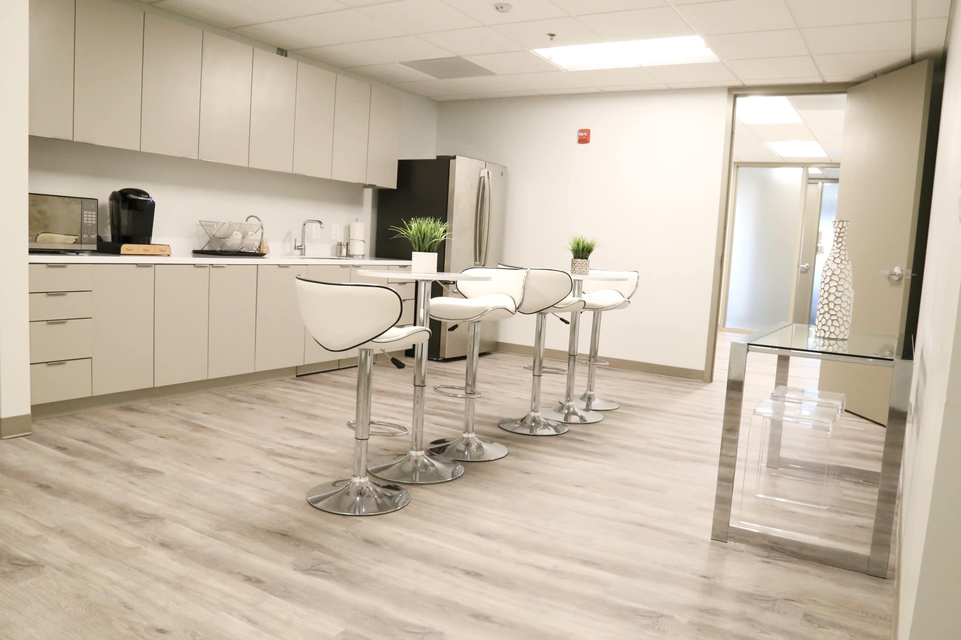 The image shows a modern kitchen area with a breakfast bar, four white stools, and stainless steel appliances.