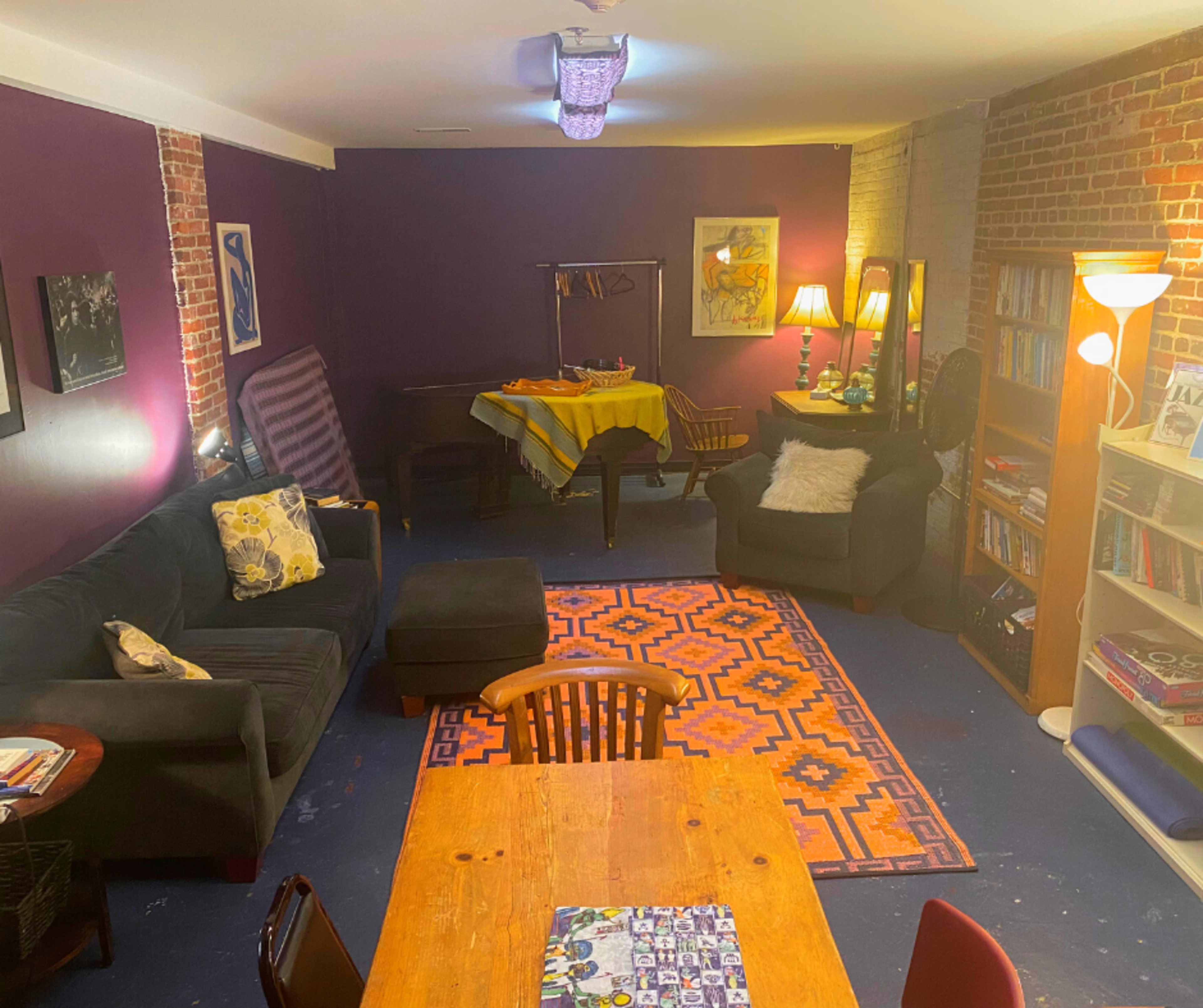 A cozy living space with purple walls, a wooden dining table, a dark sofa, and bookshelves filled with books.