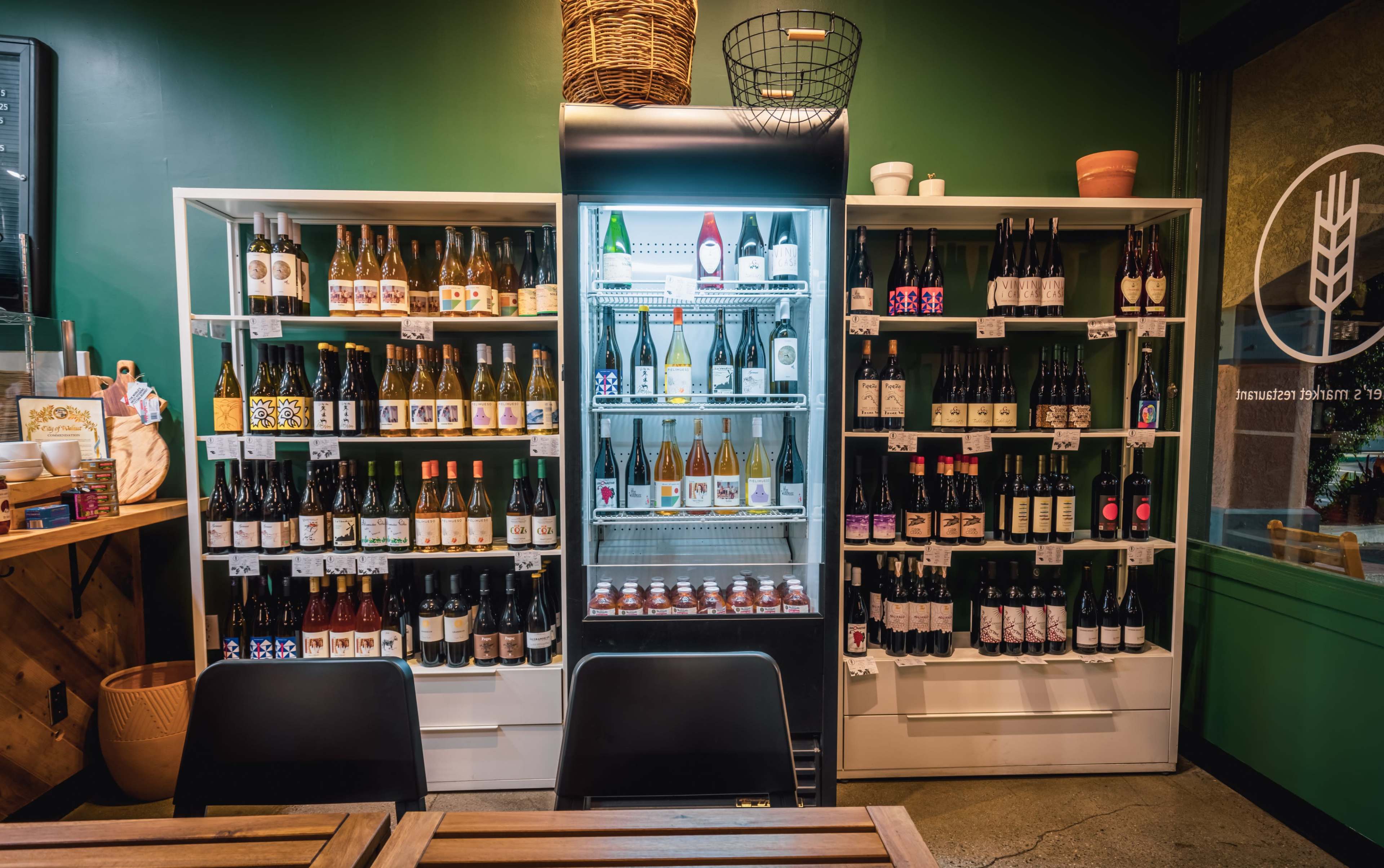 The image shows a refrigerated display surrounded by shelves filled with various bottles of wine arranged neatly against a green wall.
