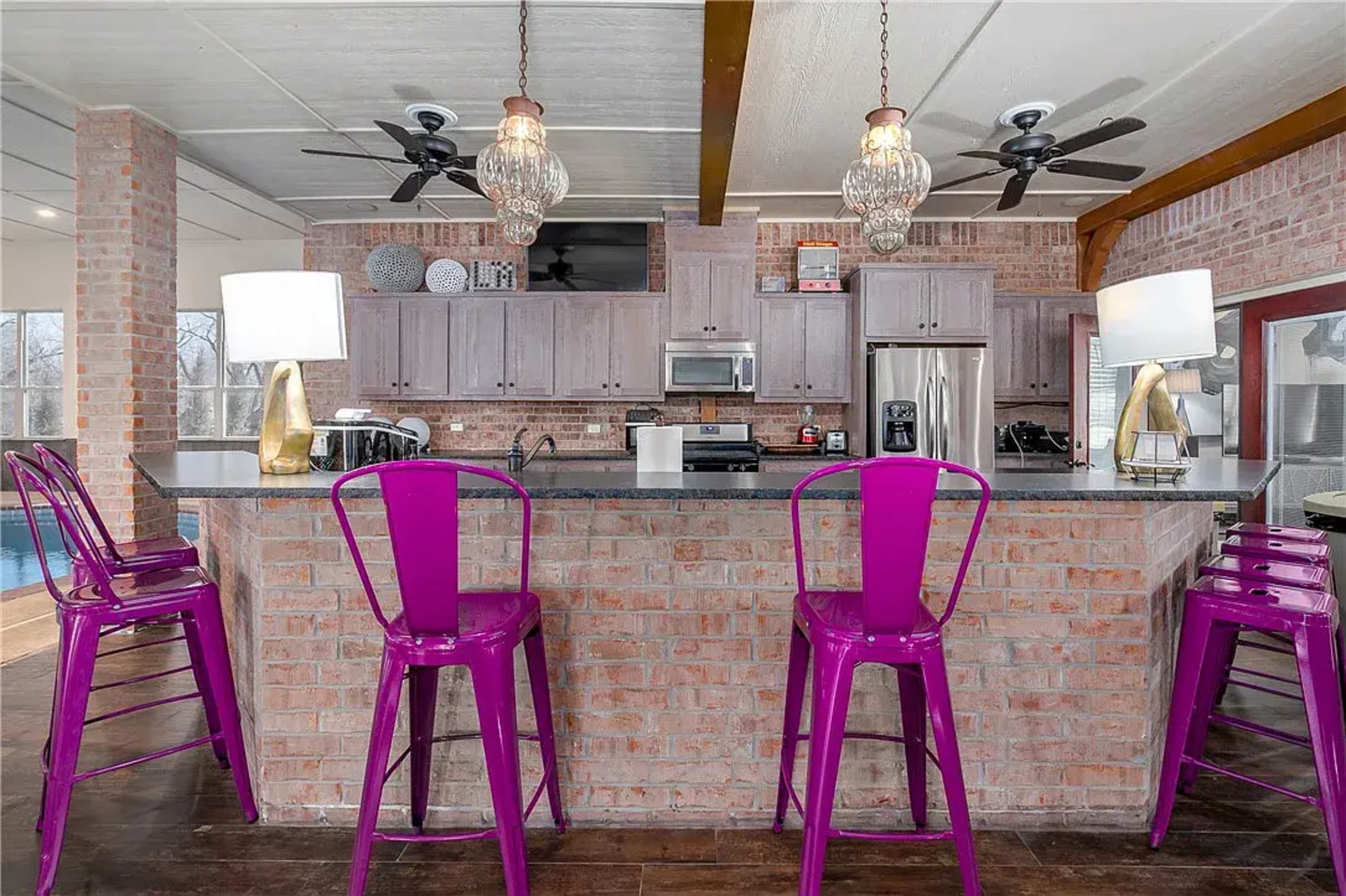 A modern kitchen with a brick island and four purple metal bar stools.