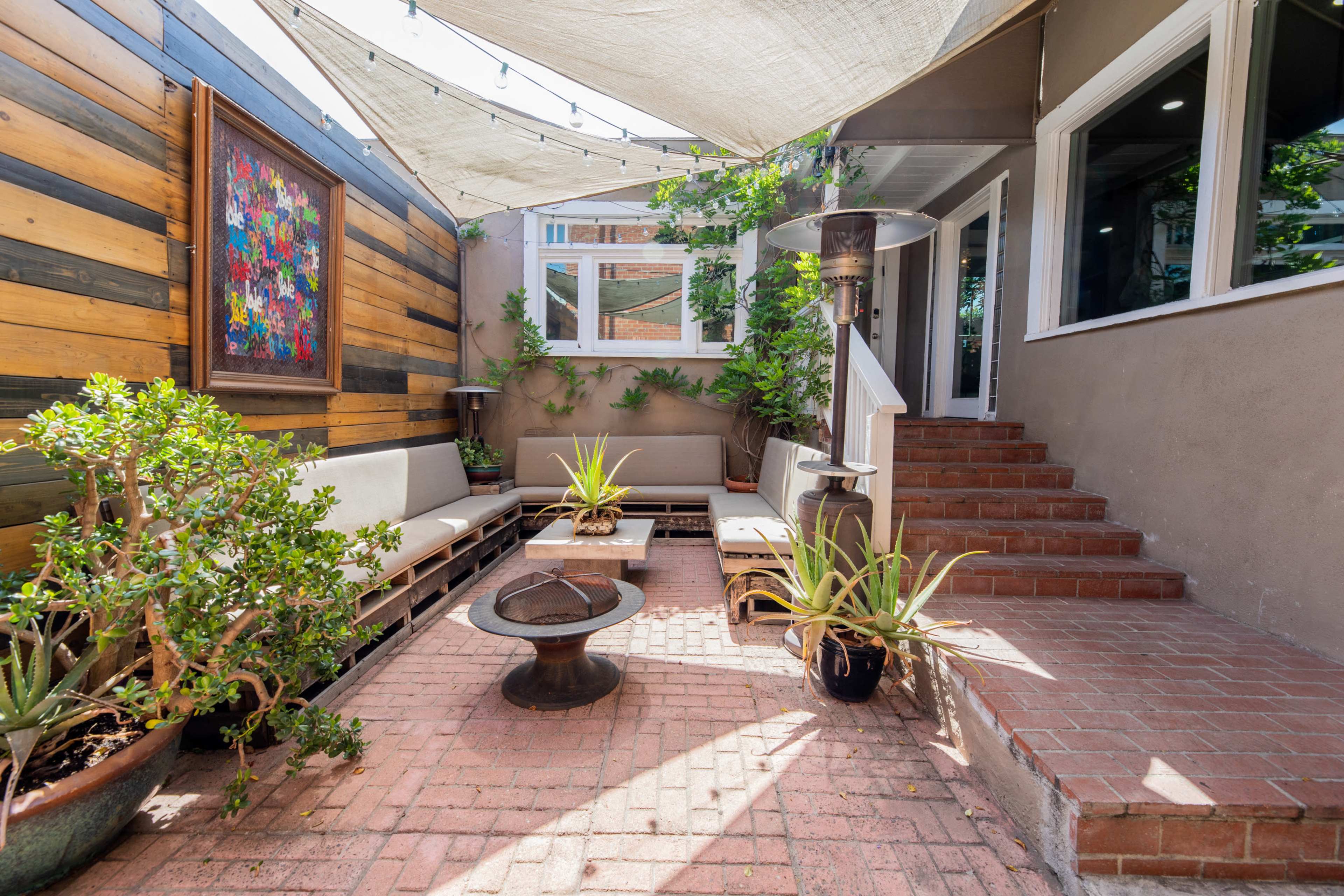 A patio area featuring a covered seating arrangement, a fire pit, potted plants, and steps leading to an interior space.