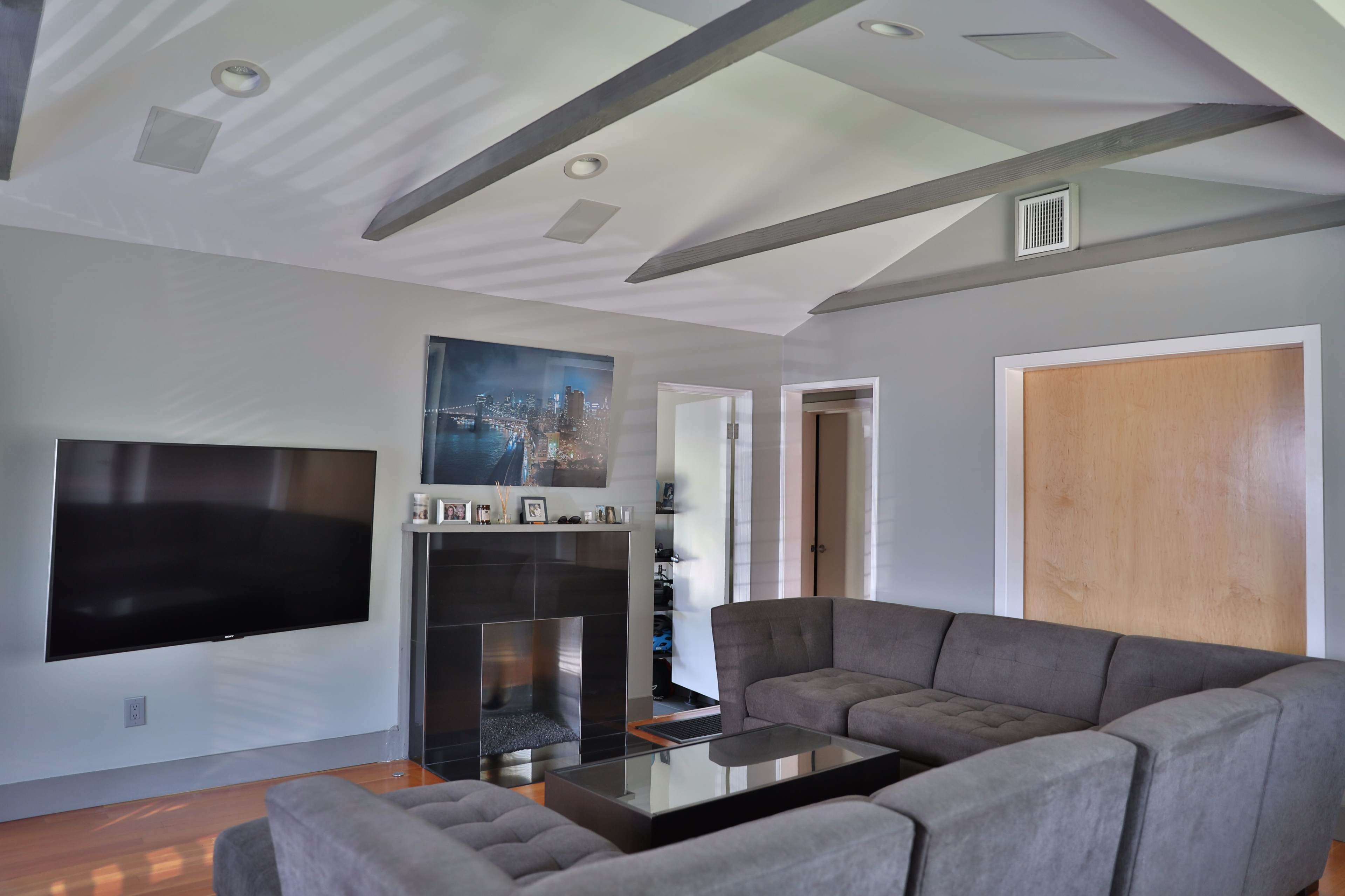 The image shows a modern living room with a large sectional sofa, a flat-screen TV mounted on the wall, and a fireplace beneath a piece of artwork.