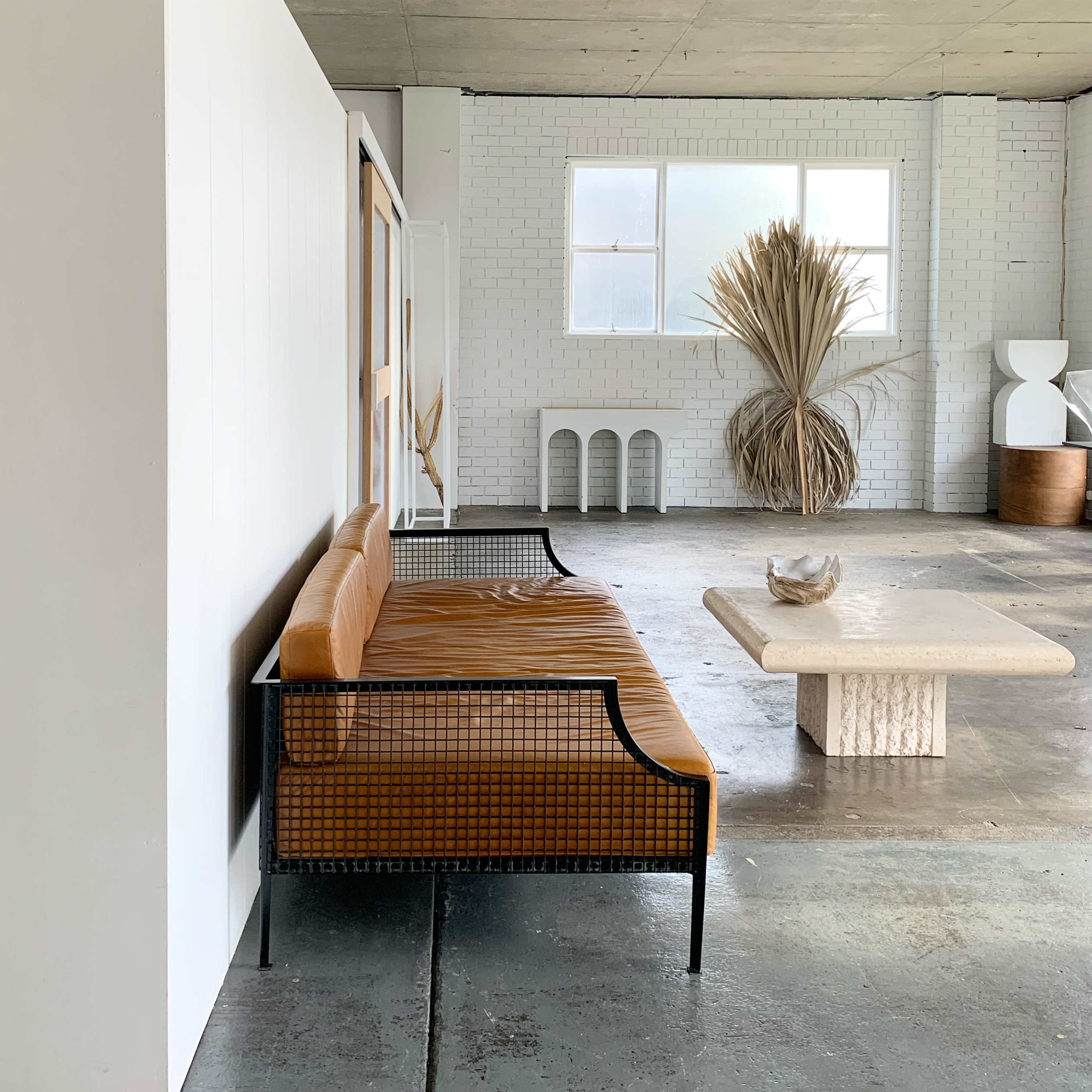 A modern living space features a leather sofa and a stone coffee table, with dried plants in the background.