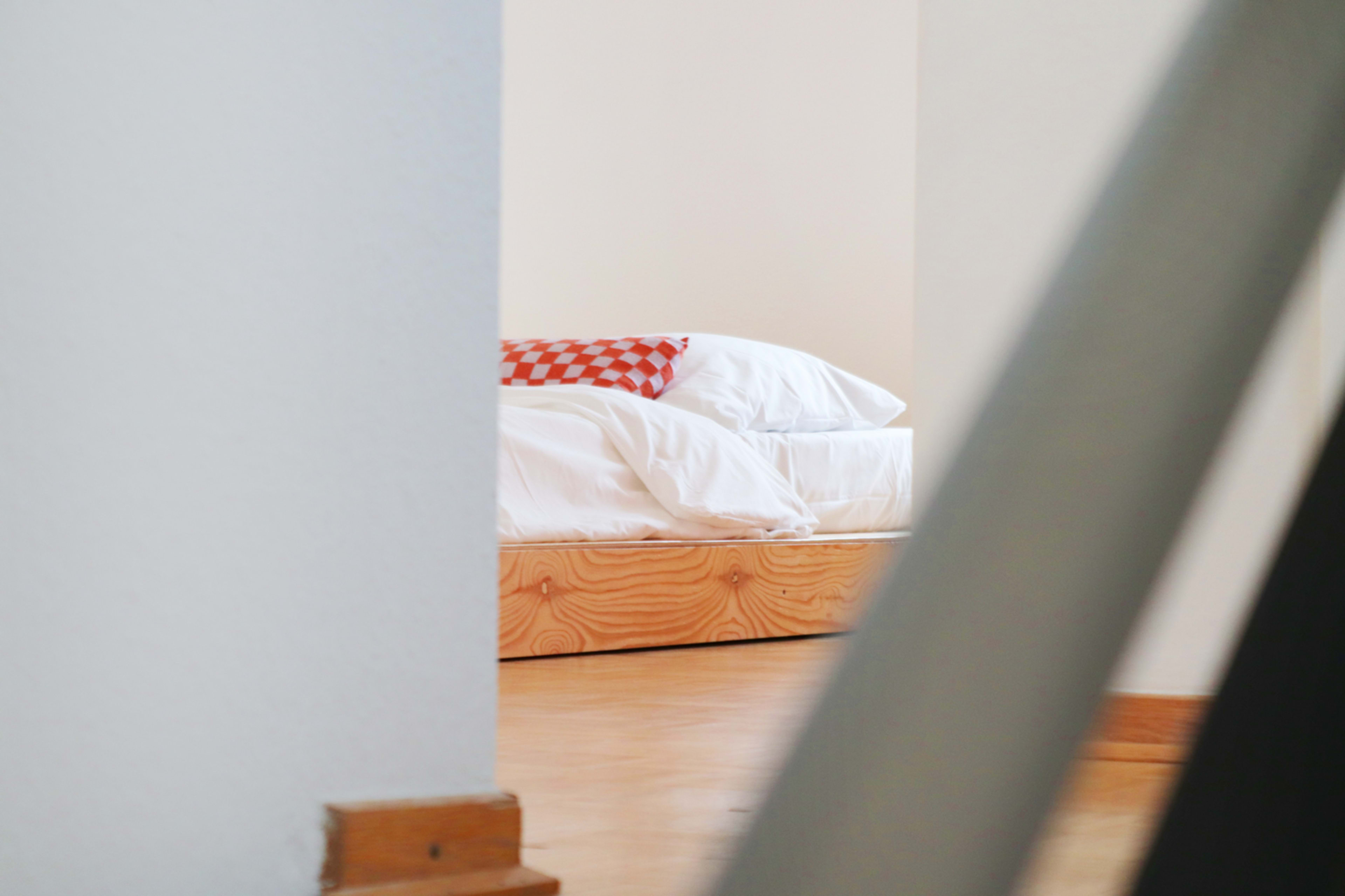 A neatly made bed with white bedding and an orange checkered pillow is visible through a doorway.