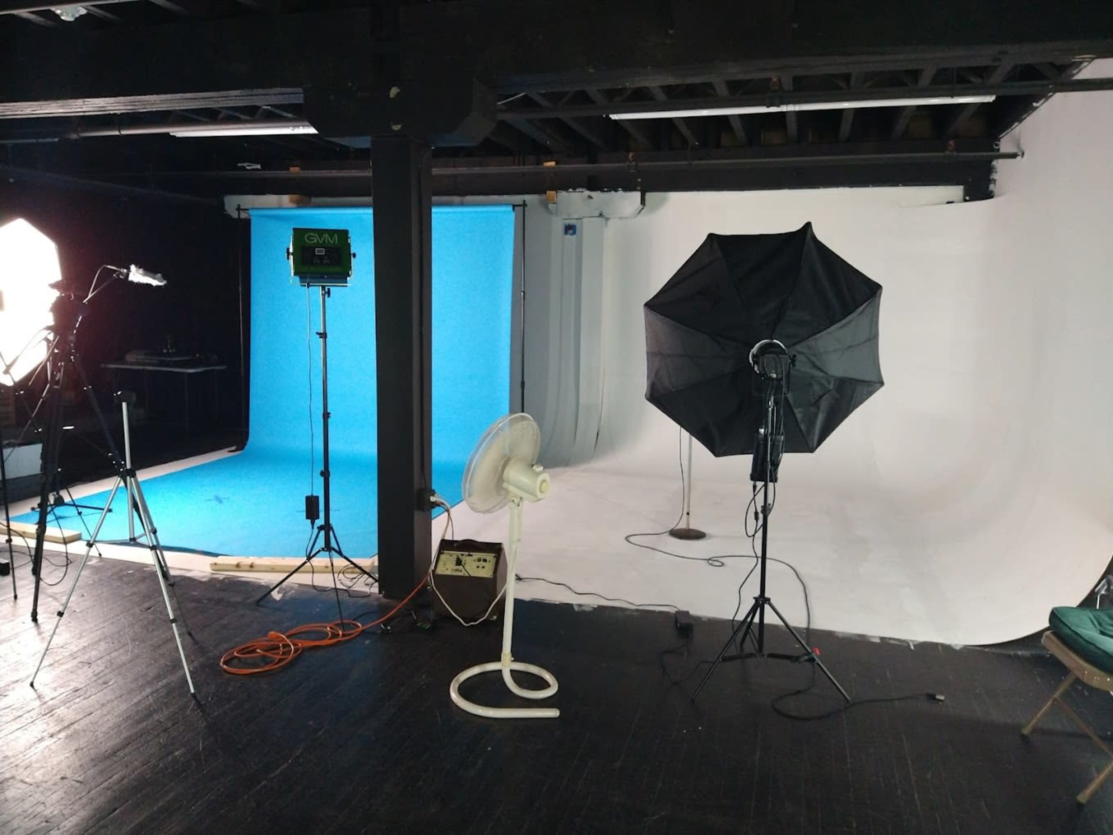 A photography studio with two backdrop screens, one blue and one white, along with various lighting equipment and a standing fan.