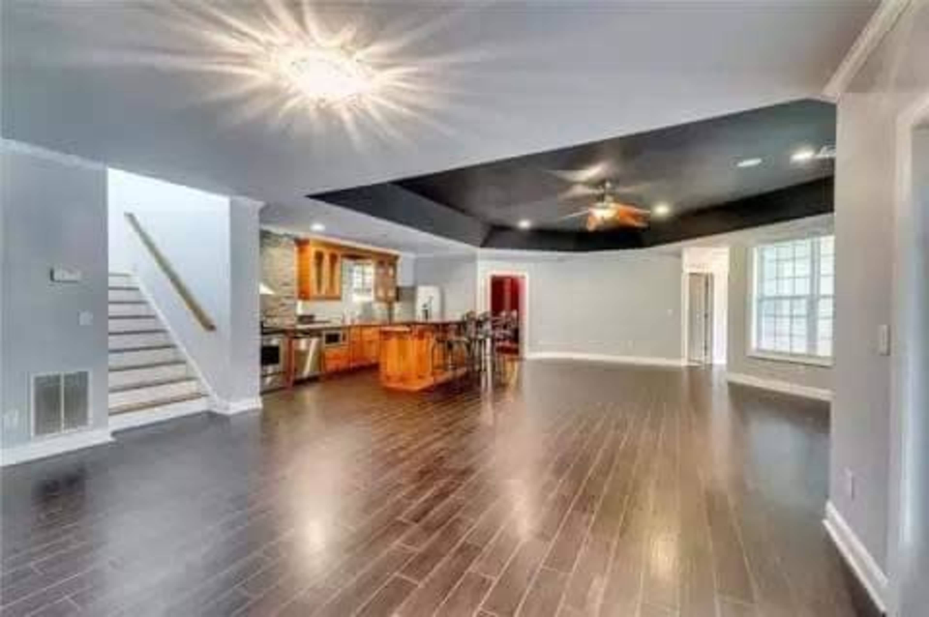 A spacious interior living area with dark wood flooring, a kitchen in the background, and a staircase leading to another level.