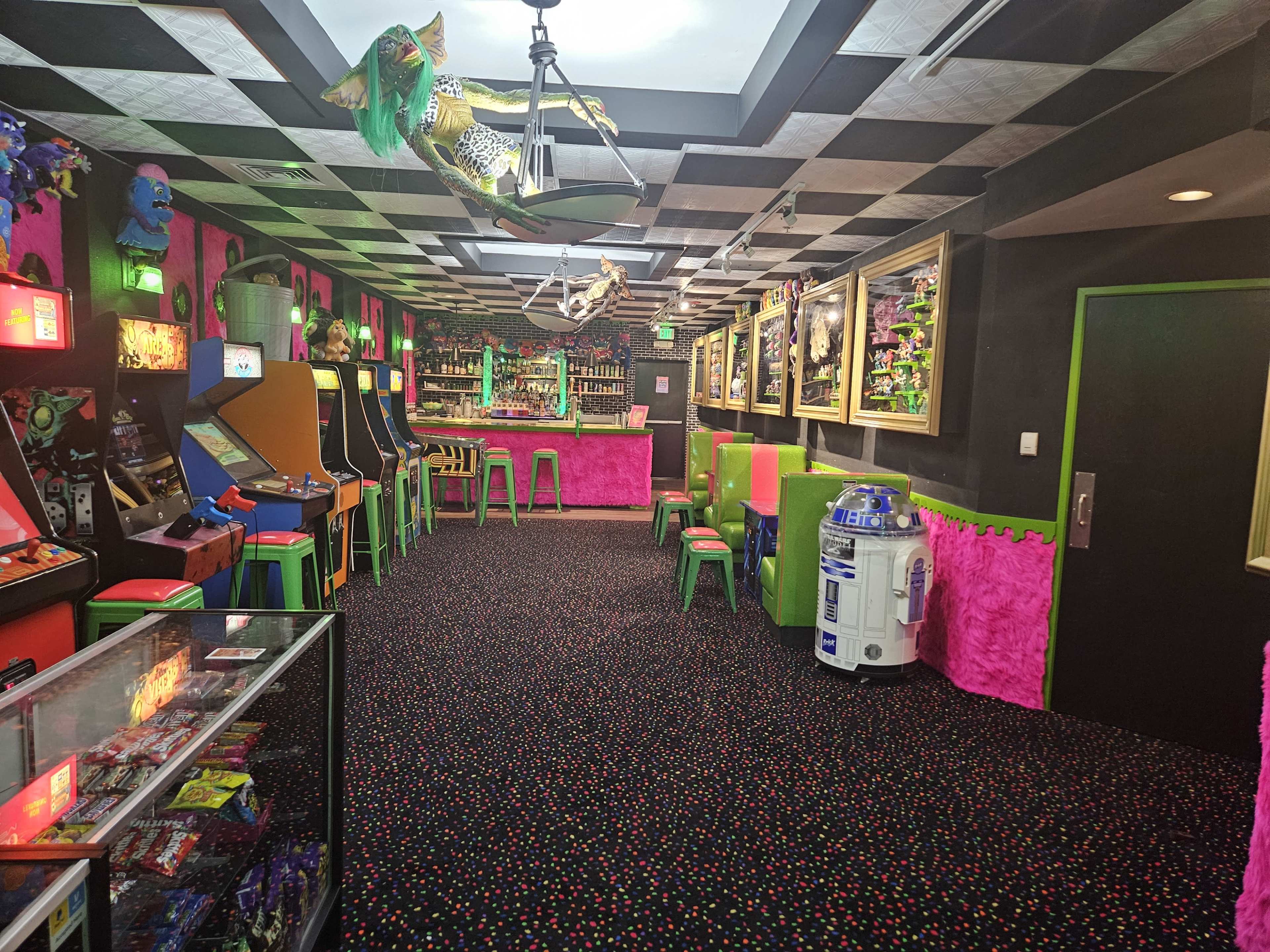 The image shows an arcade with colorful walls, retro arcade machines, and a bar area, all illuminated by bright lights.
