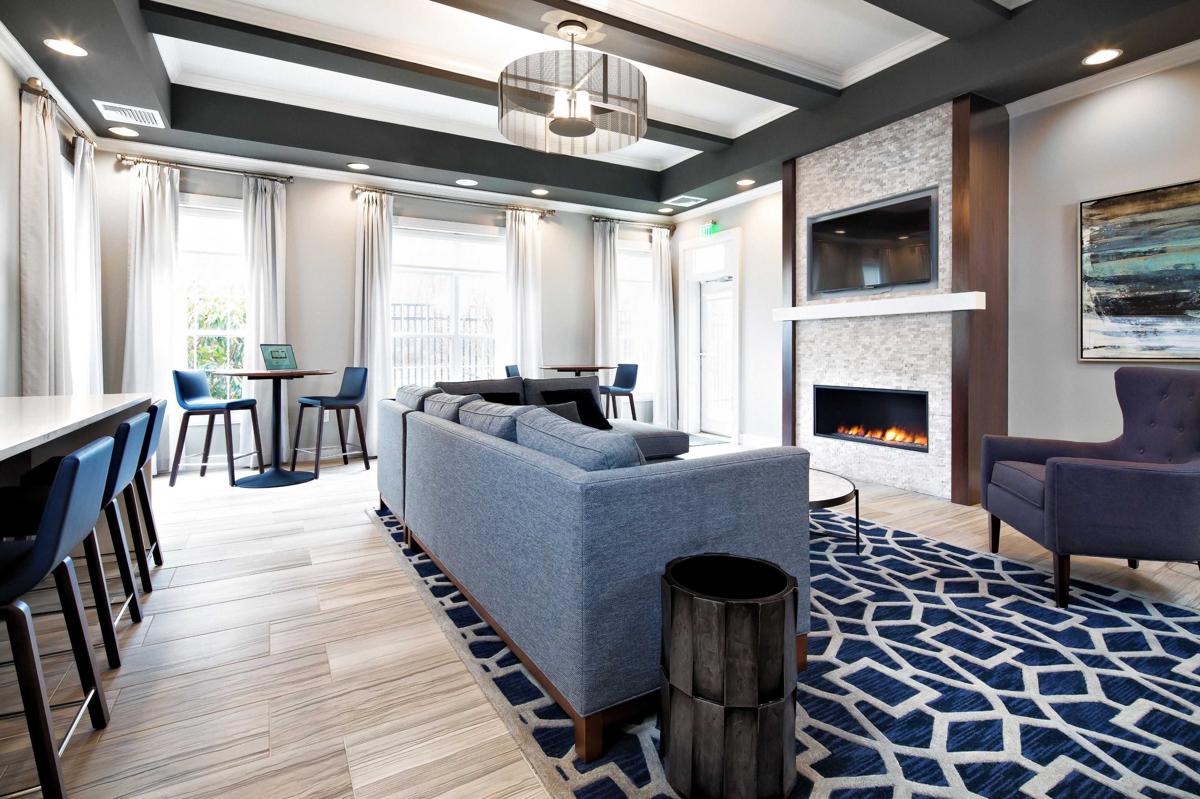 A modern lounge area features a blue sofa, a stone fireplace, and large windows allowing natural light to fill the space.