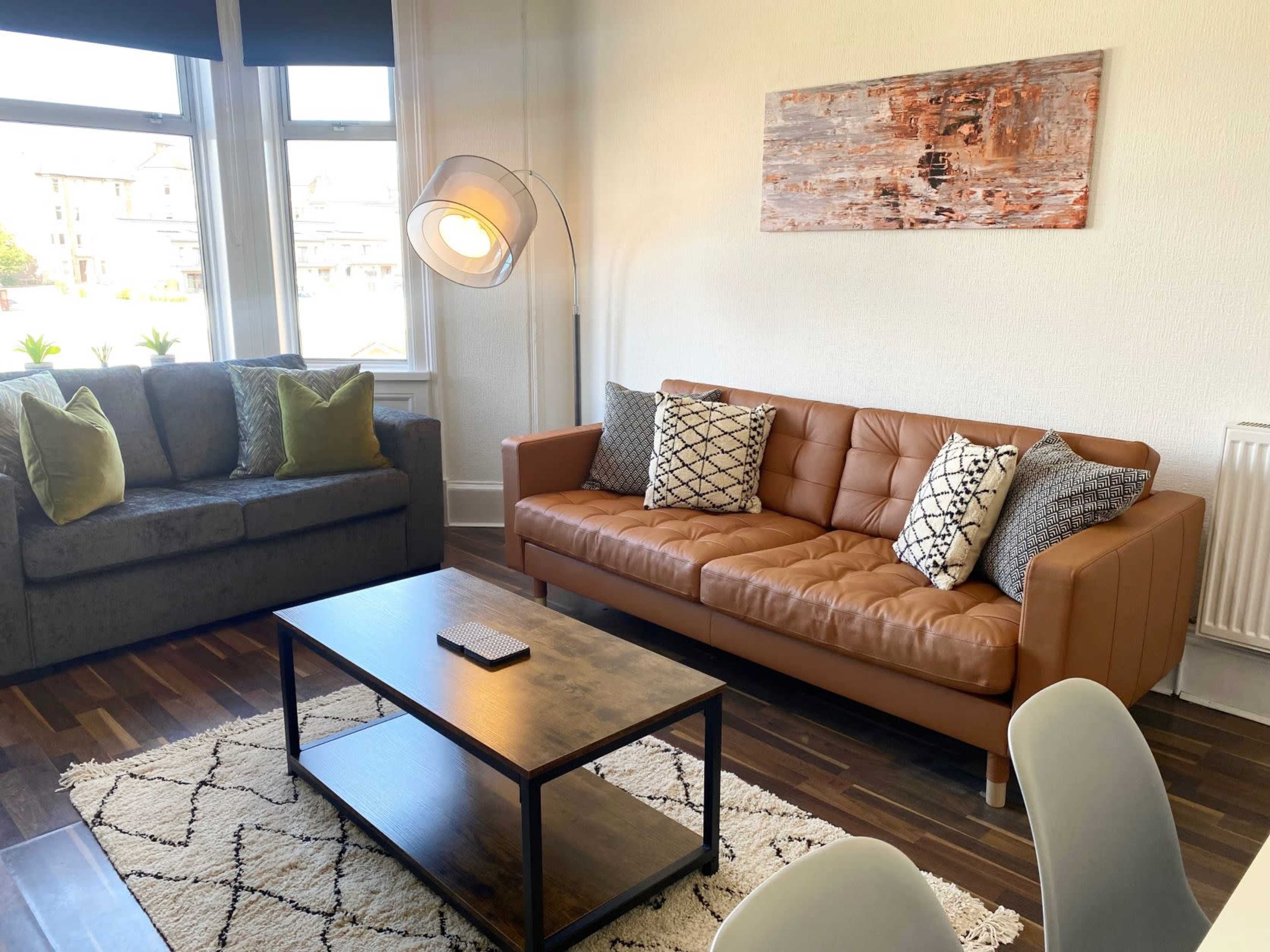 A modern living room with a brown leather sofa, a gray couch, a wooden coffee table, and a patterned rug.