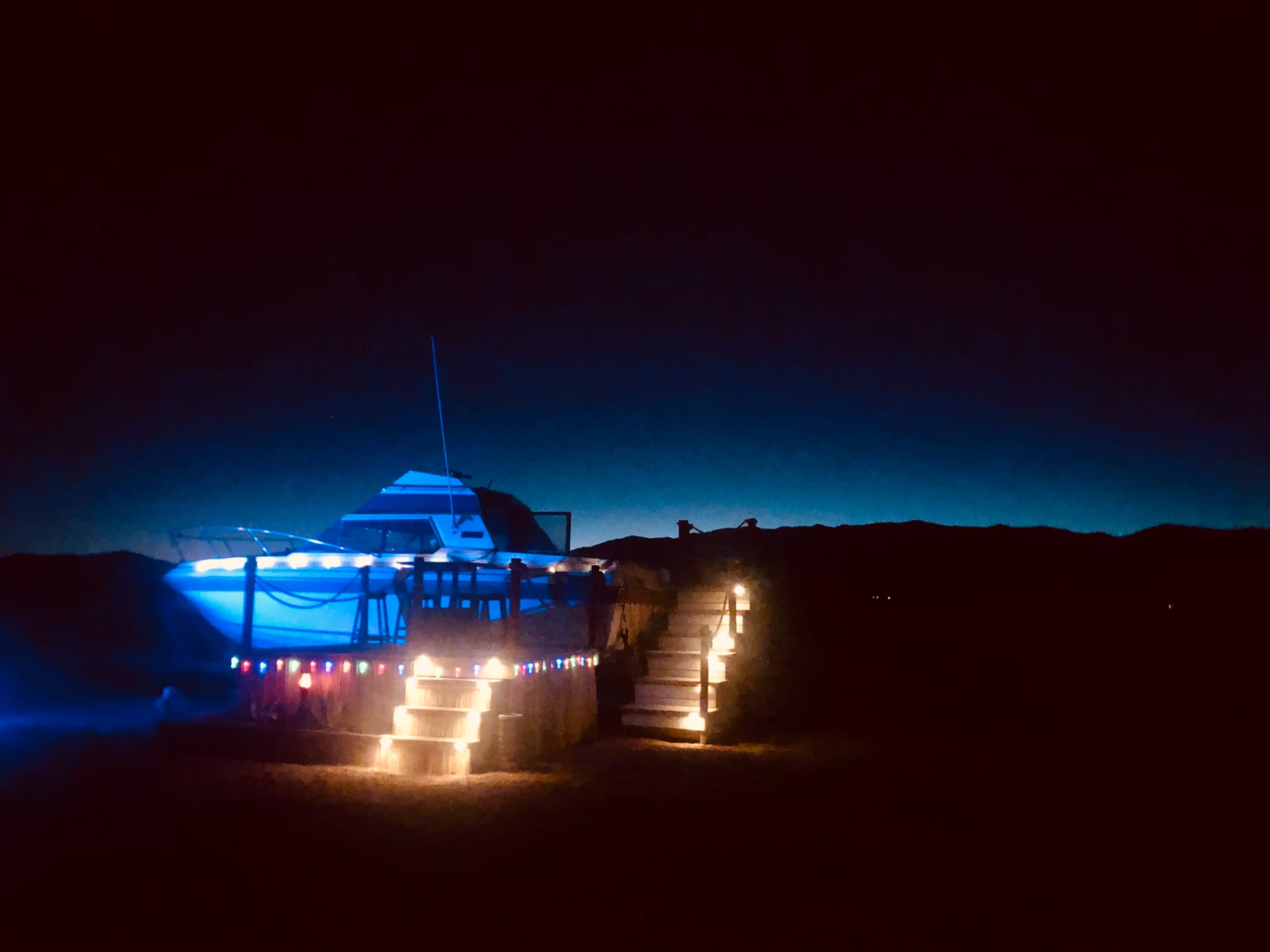 A brightly lit boat is docked on a platform decorated with colorful lights against a dark, mountainous backdrop.