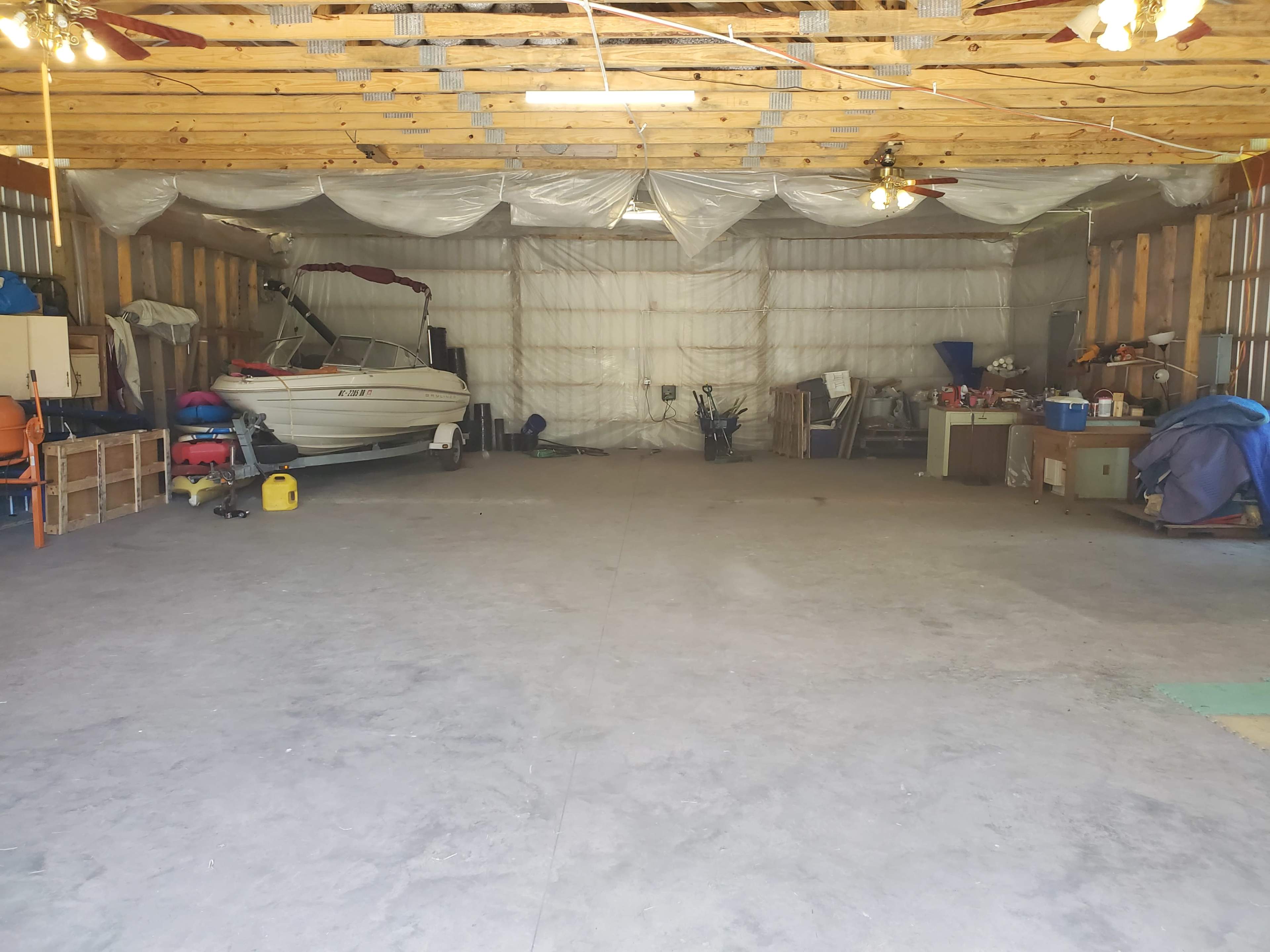 A large, empty garage features a boat on one side and assorted tools and equipment against the walls.