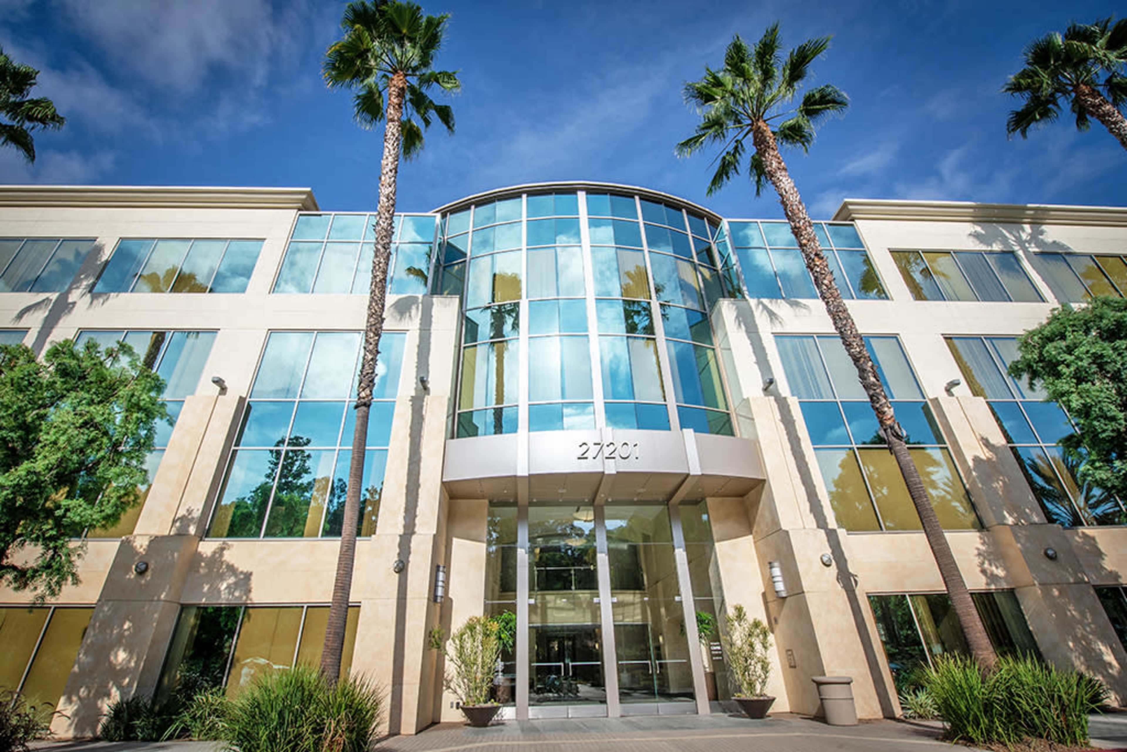A modern glass-fronted office building surrounded by palm trees.
